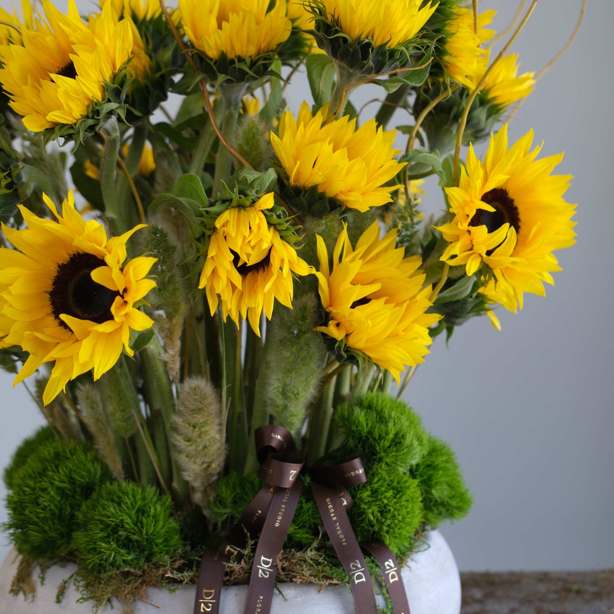 Yellow sunflowers arranged in a white bowl vase with brown ribbons