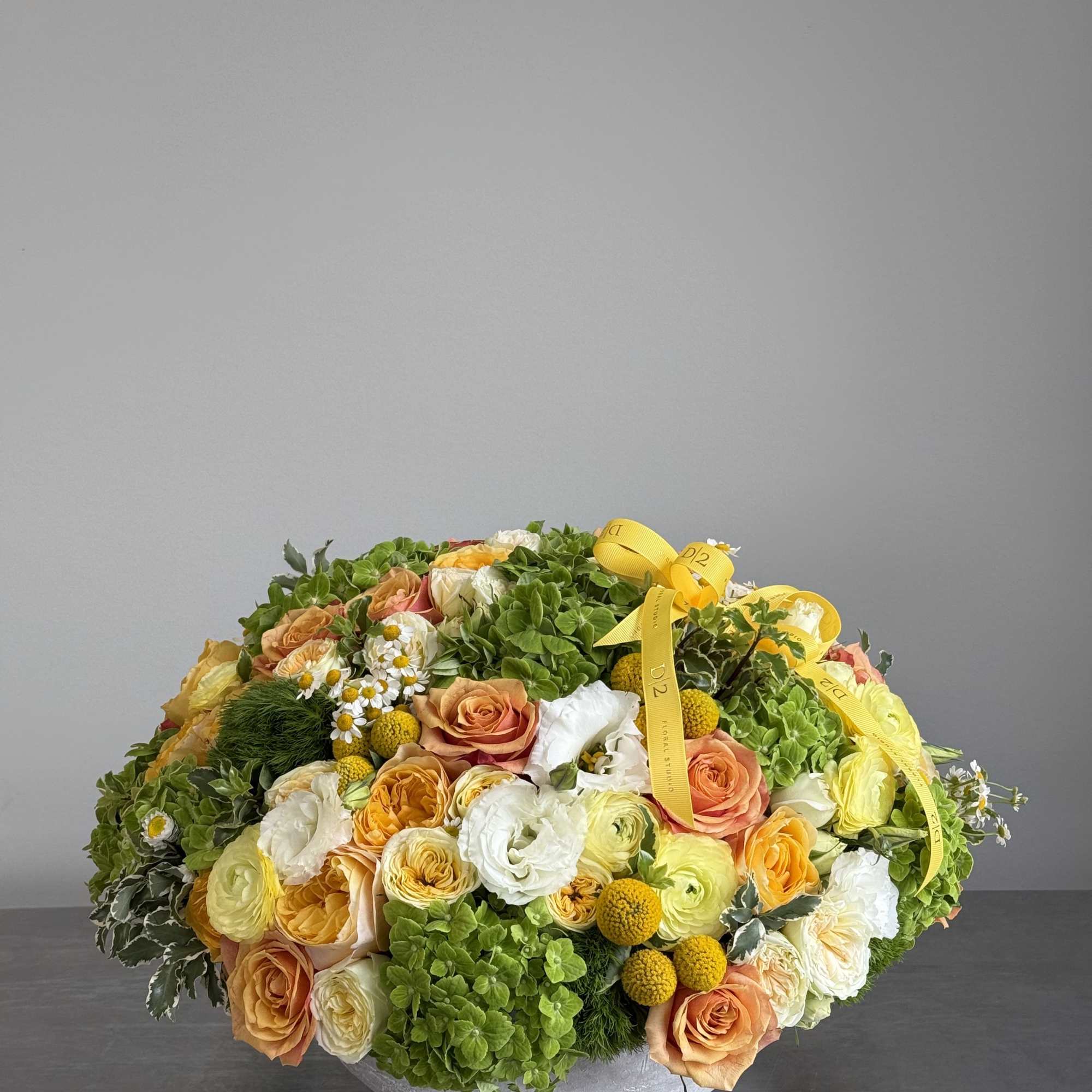 Round floral arrangement with peach and white roses in a low gray bowl