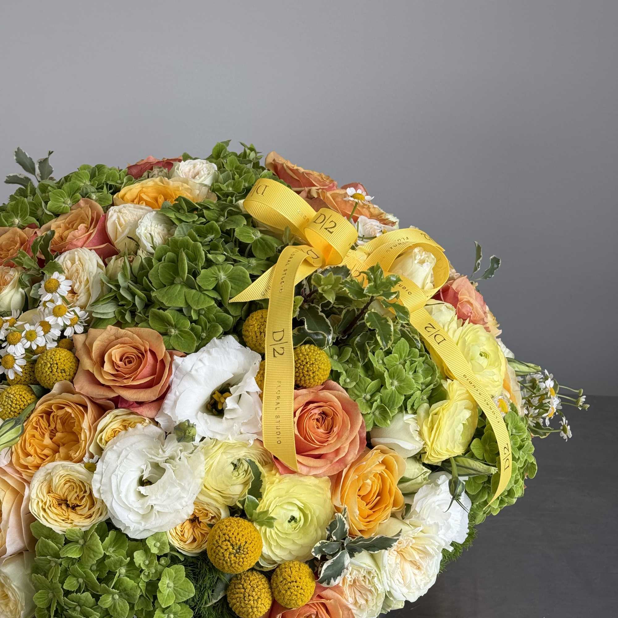 Round bouquet of peach, white, and yellow flowers with yellow ribbon