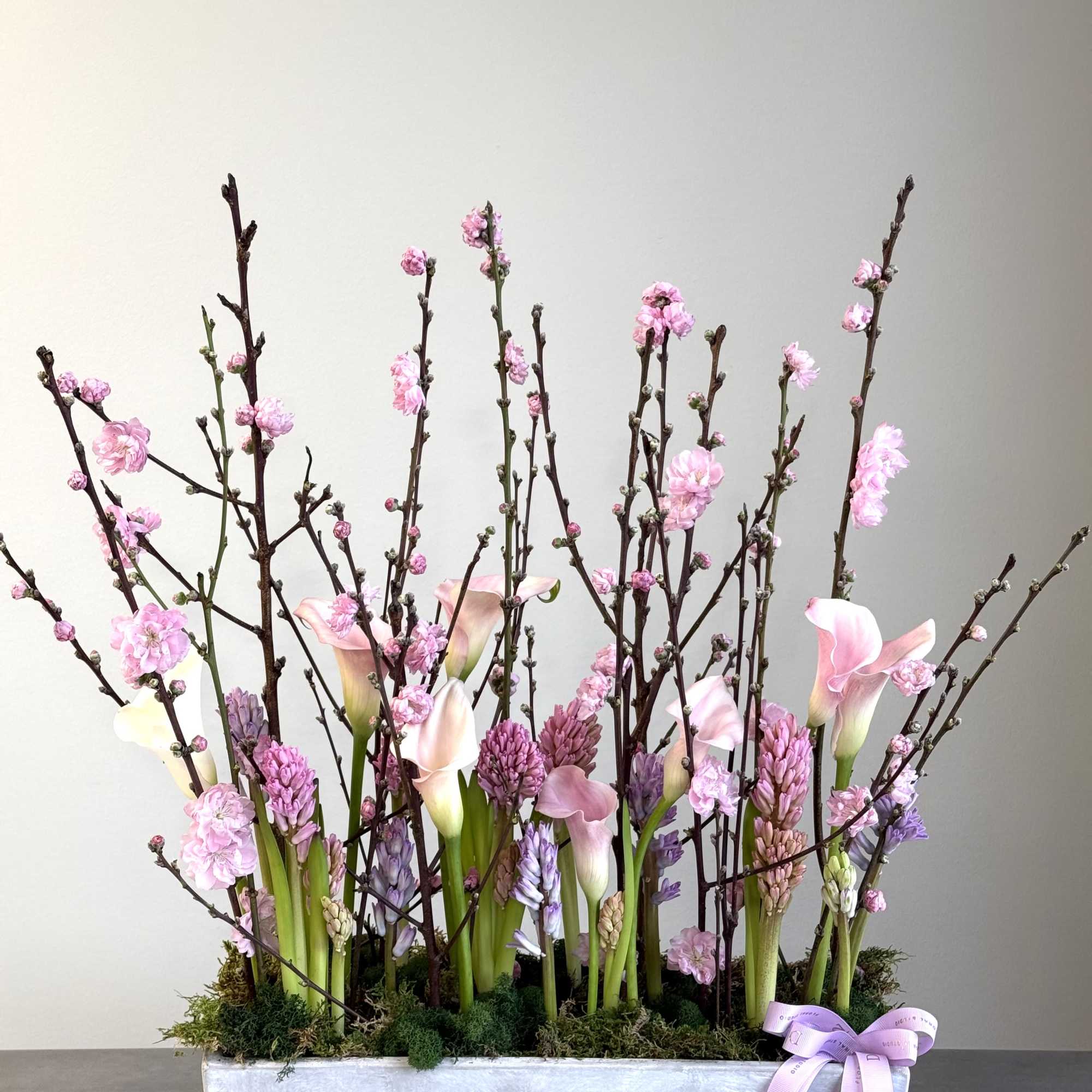 Pink calla lilies and blossoms in a rectangular silver planter