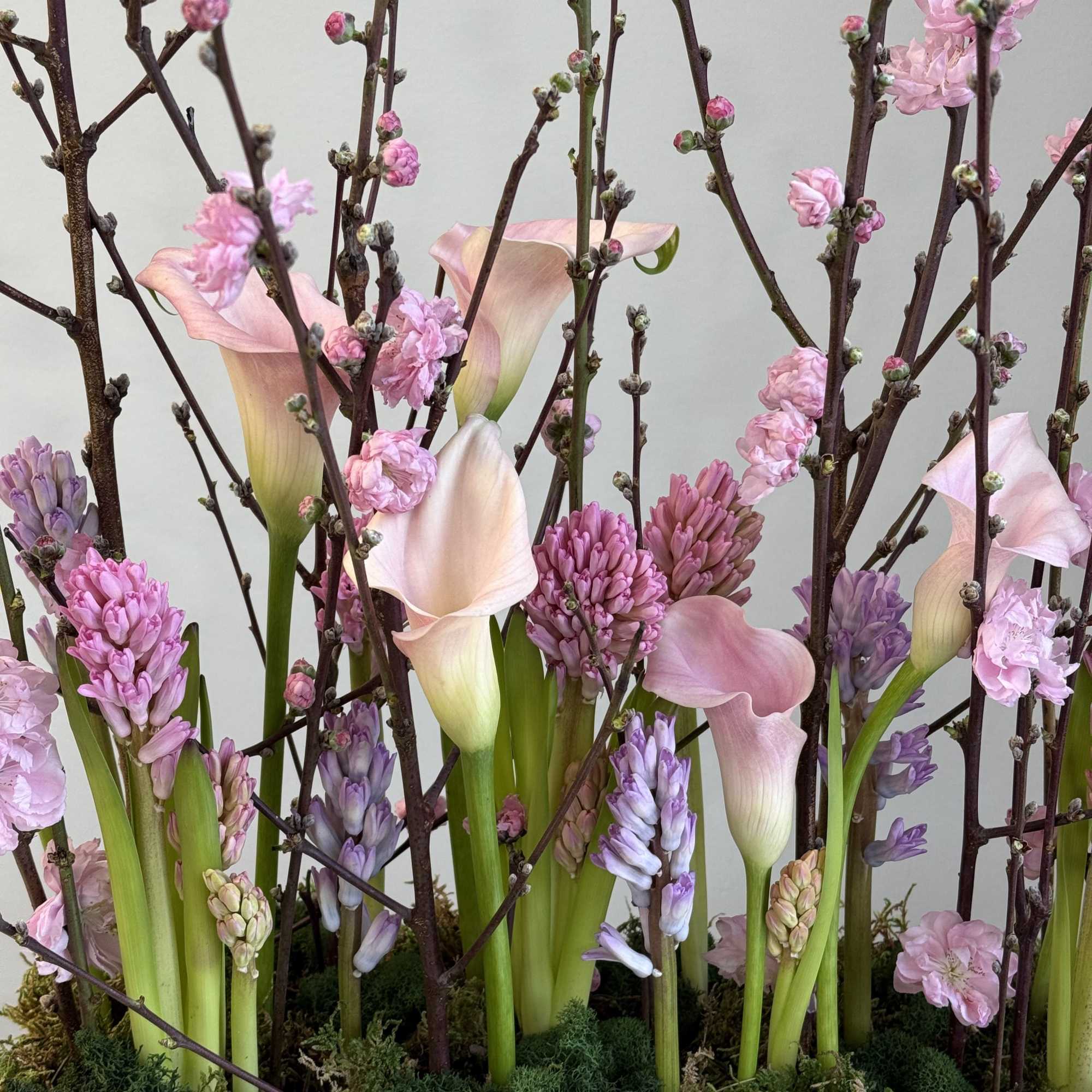 Pink calla lilies and purple hyacinths arranged with flowering branches, photo 2 of 3