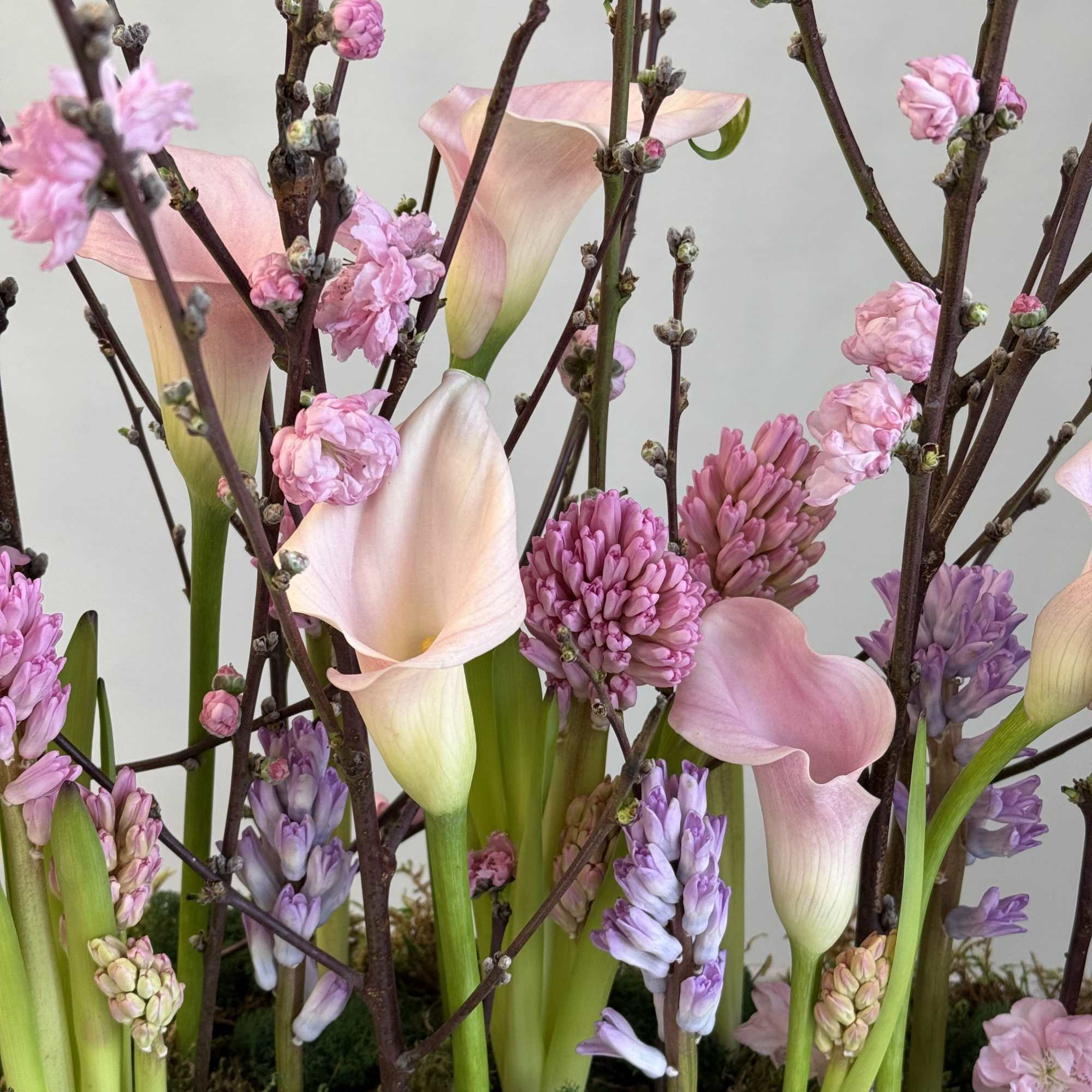 Pink calla lilies and purple hyacinths arranged with flowering branches, photo 3 of 3