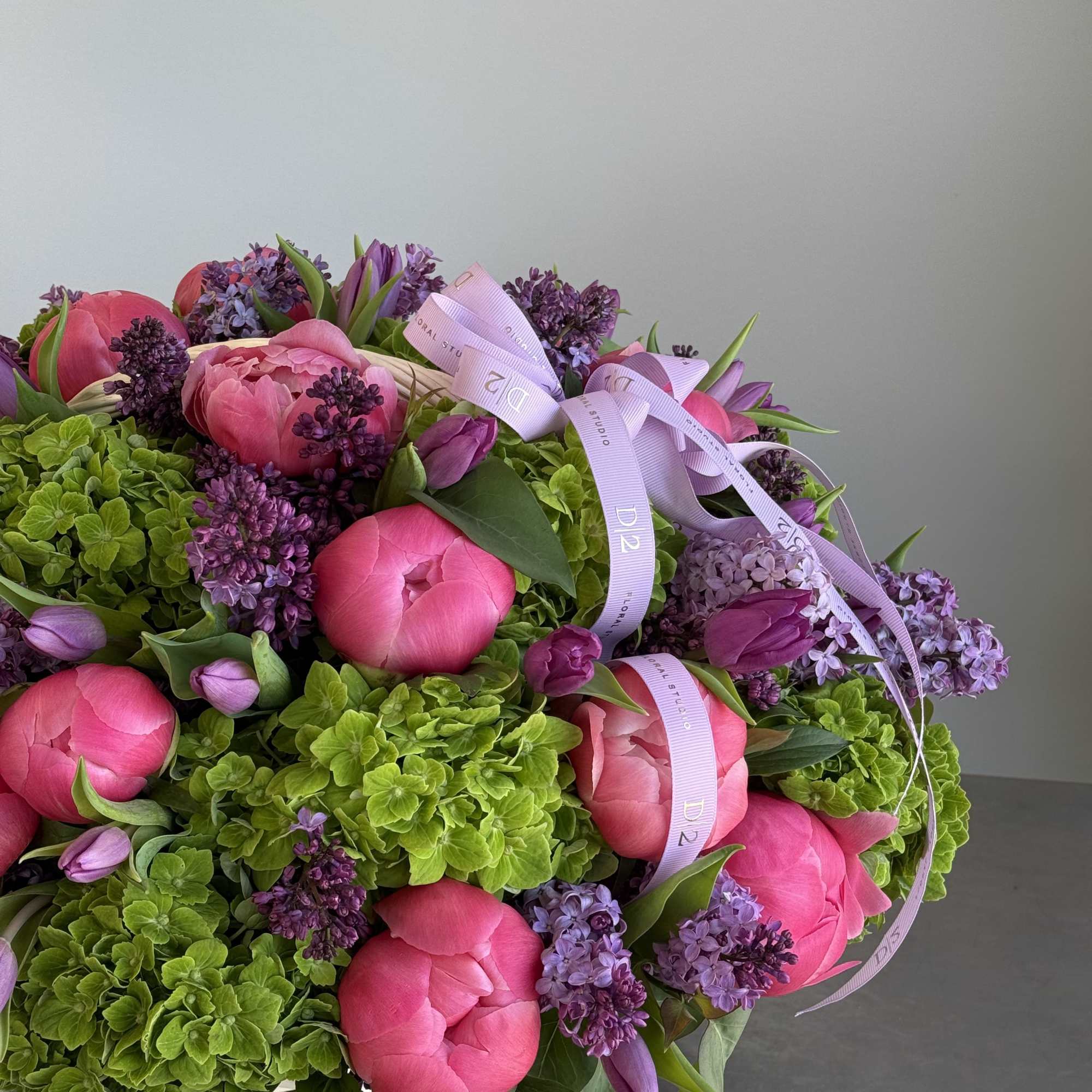 Pink peonies and purple lilacs in a white basket with ribbon