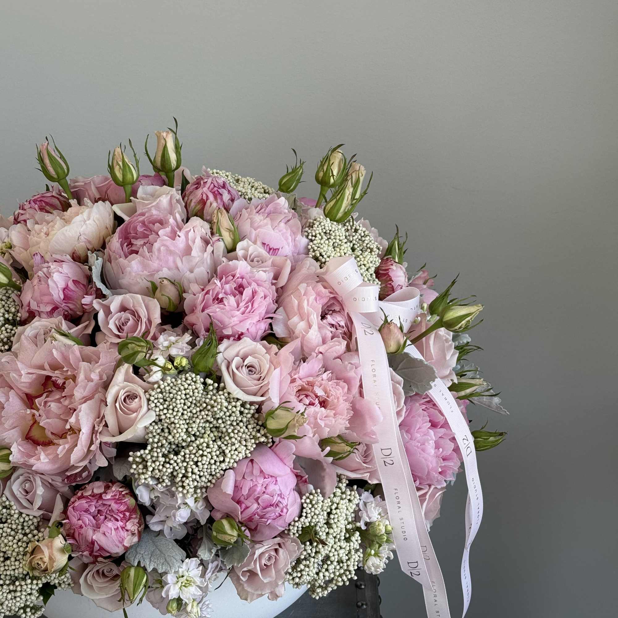 Pink peonies and roses arranged in a white vase with ribbon