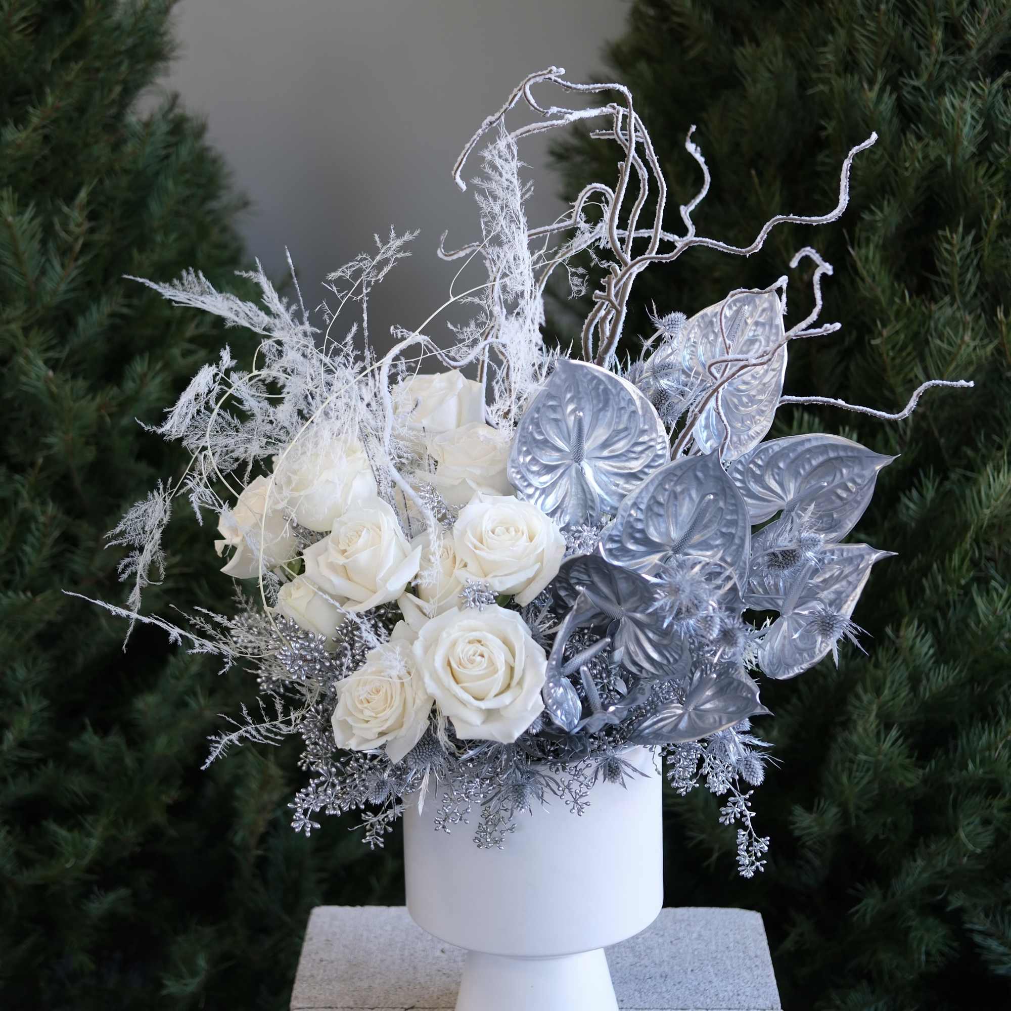 White roses in a white pedestal vase with silver decorative foliage