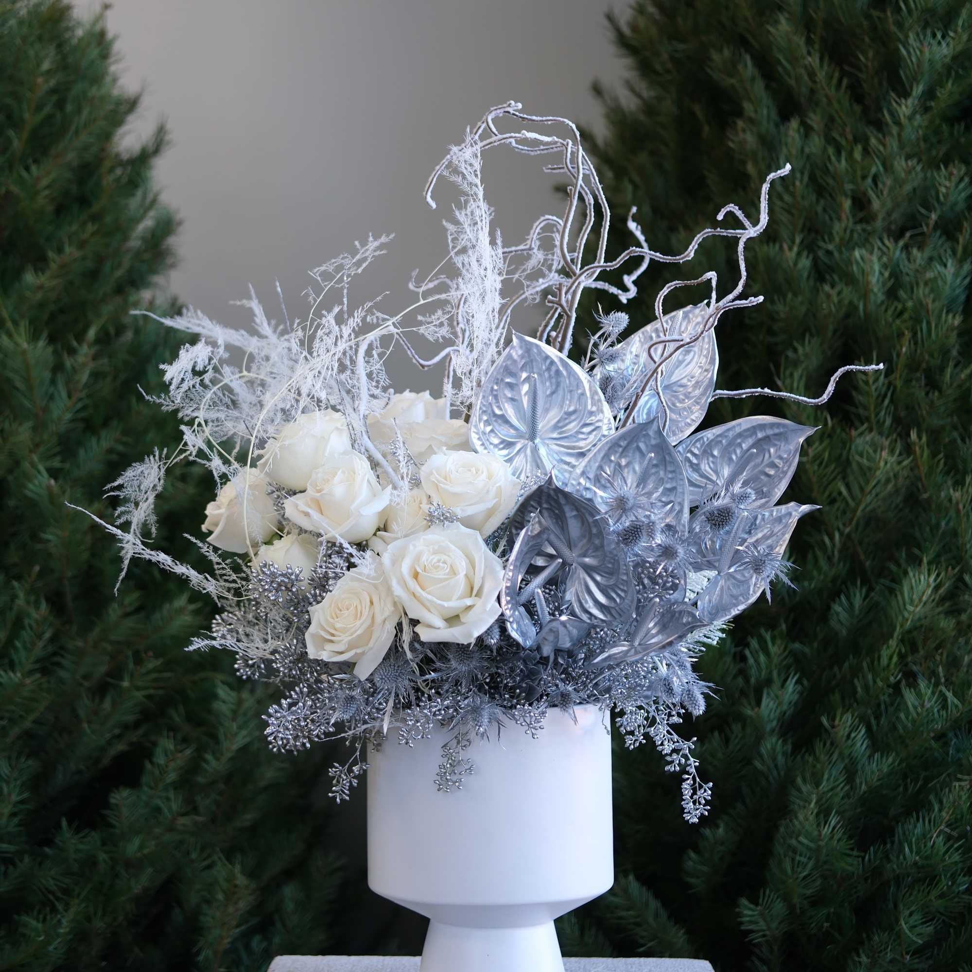 White roses and silver decorative foliage in a white pedestal vase