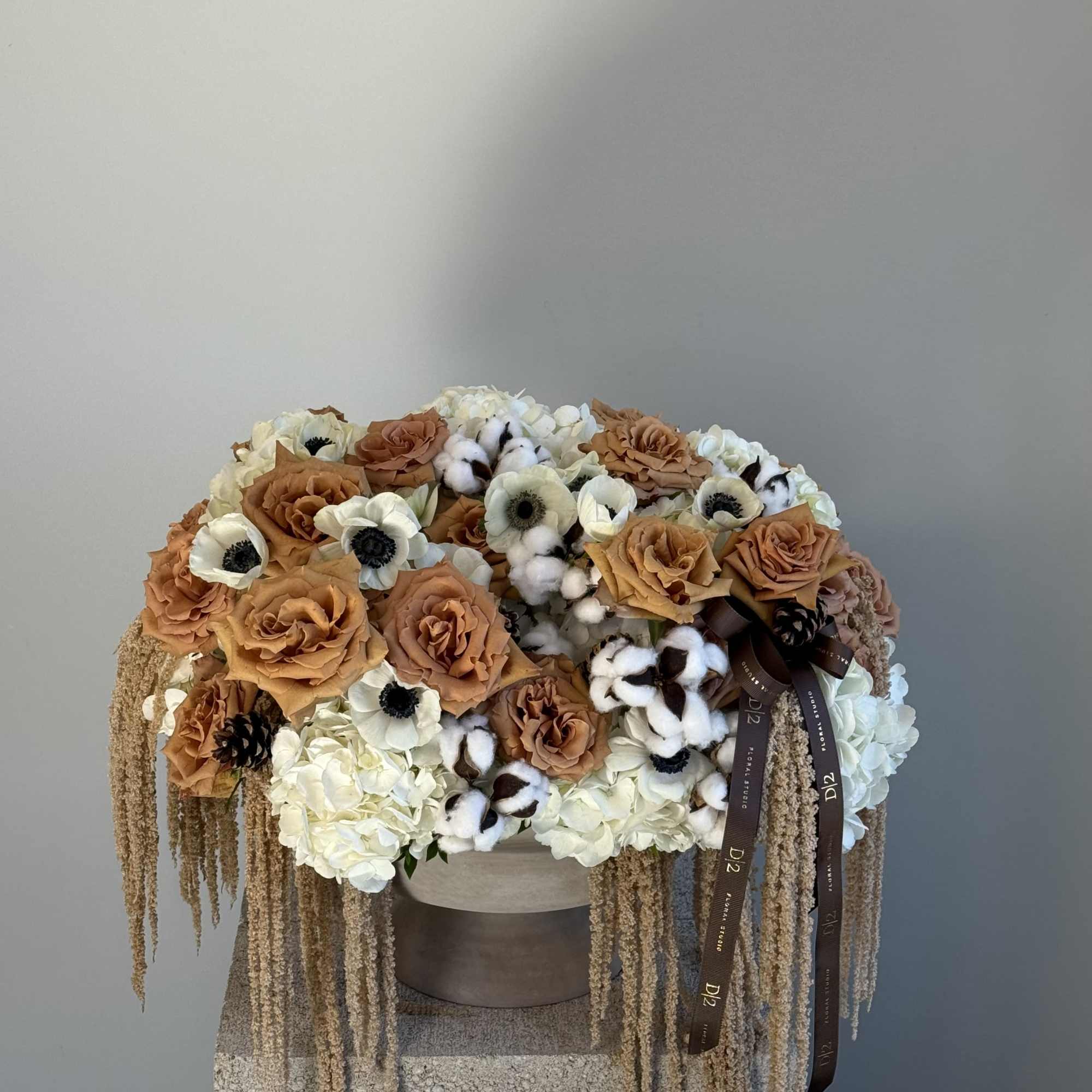 Large arrangement of tan roses, white blooms, and cotton stems in a round container