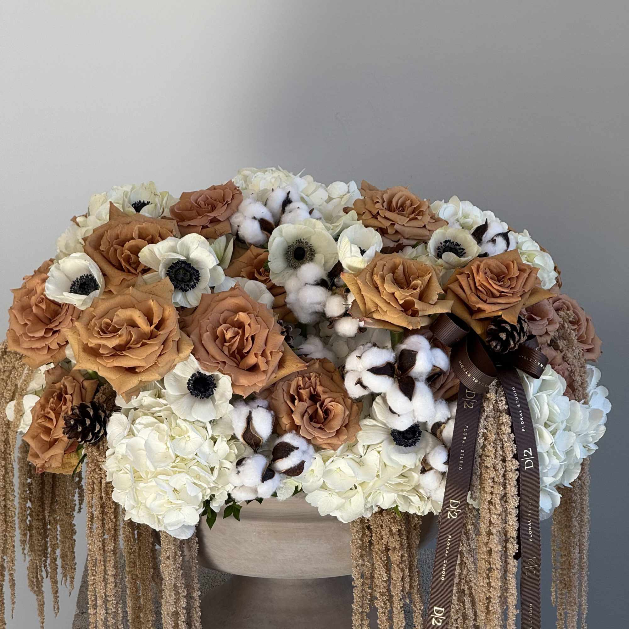 Large floral arrangement with tan roses, white anemones, and cotton stems in a vase