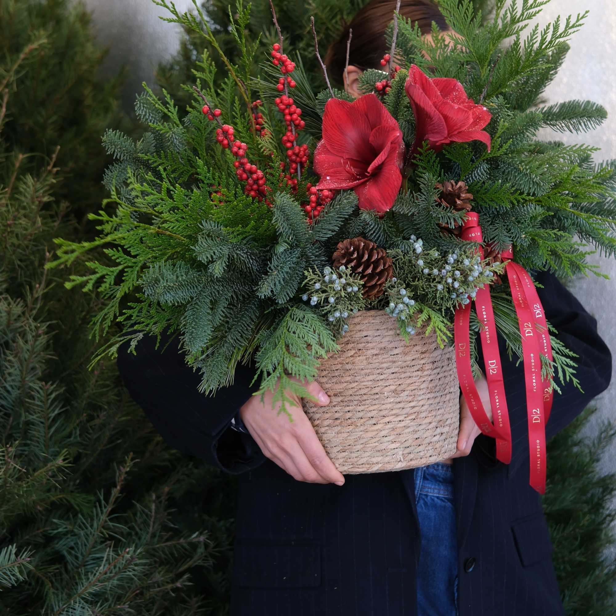 Holiday arrangement in a woven basket with red blooms and pine greenery