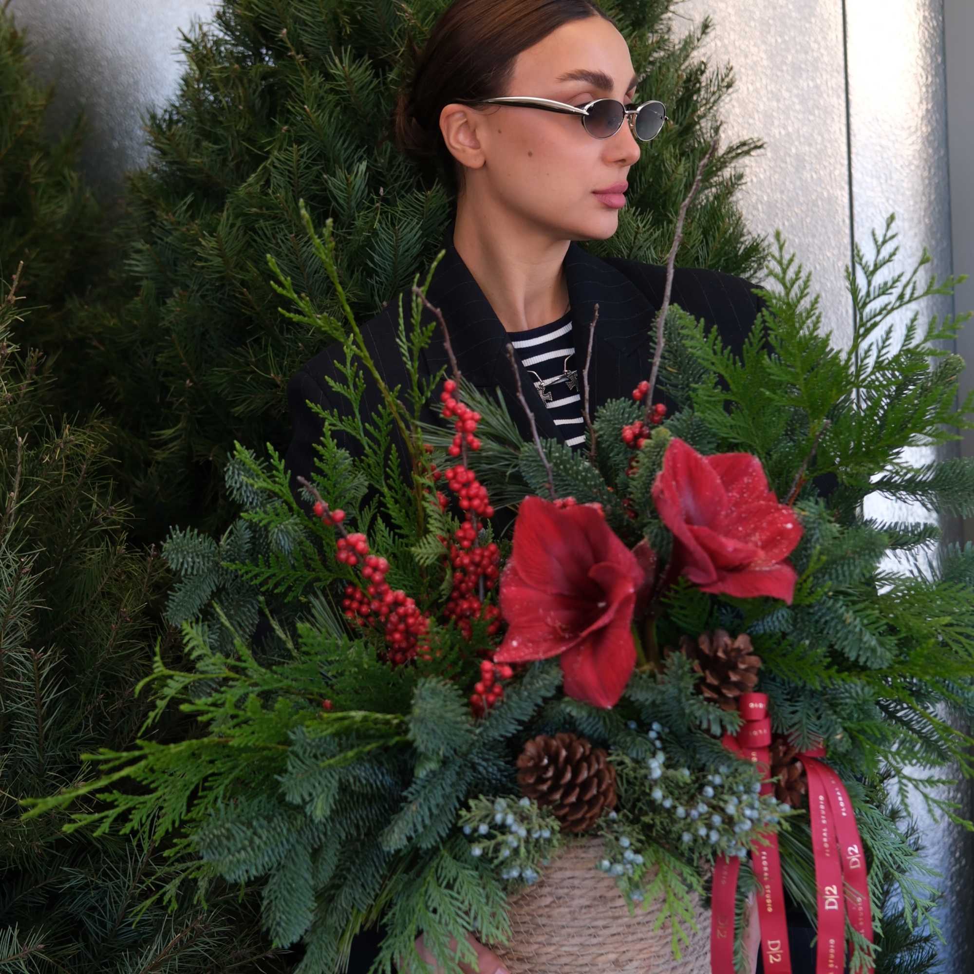 Woman holding a holiday basket arrangement with red flowers and pinecones