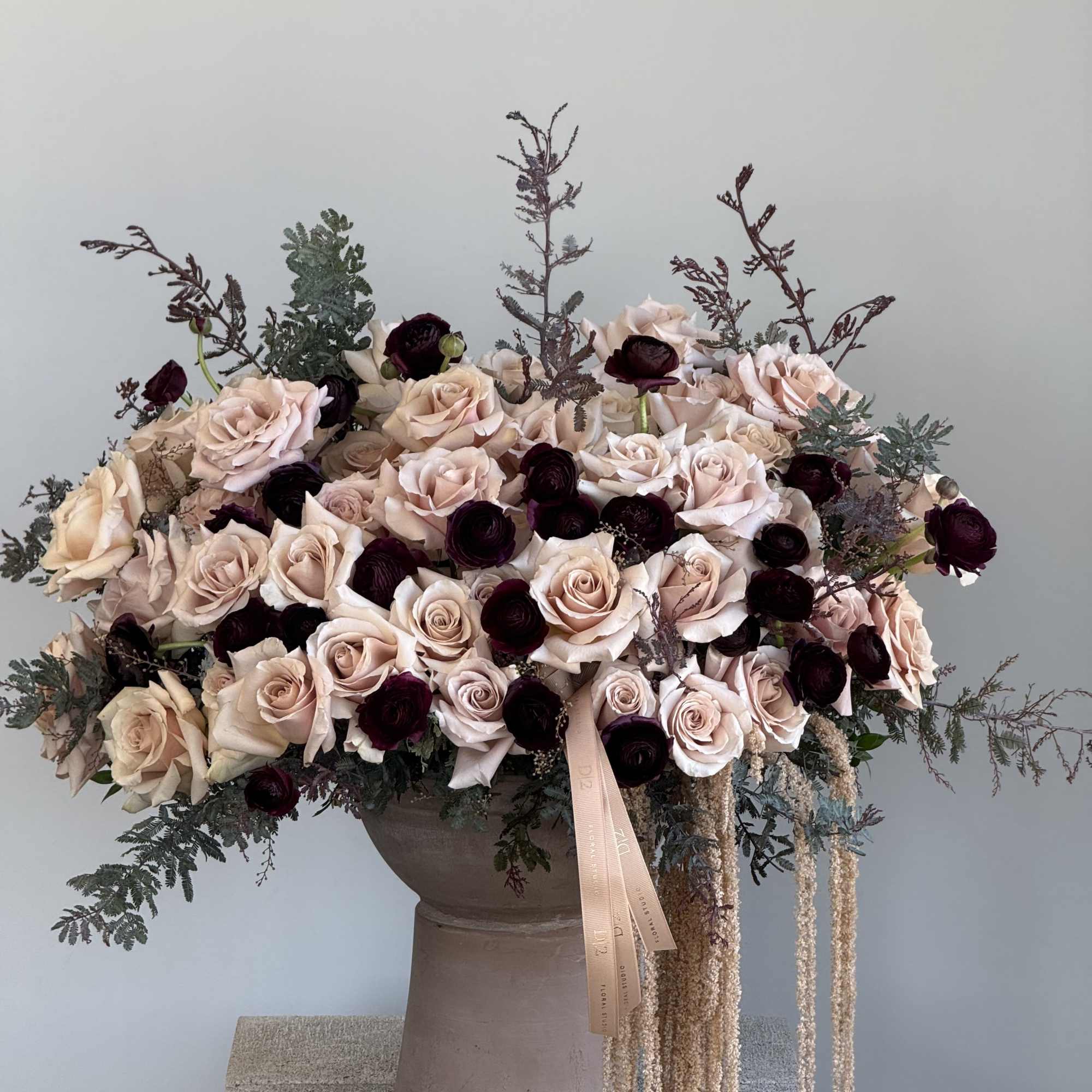 Large arrangement of blush and dark burgundy roses in a pedestal vase
