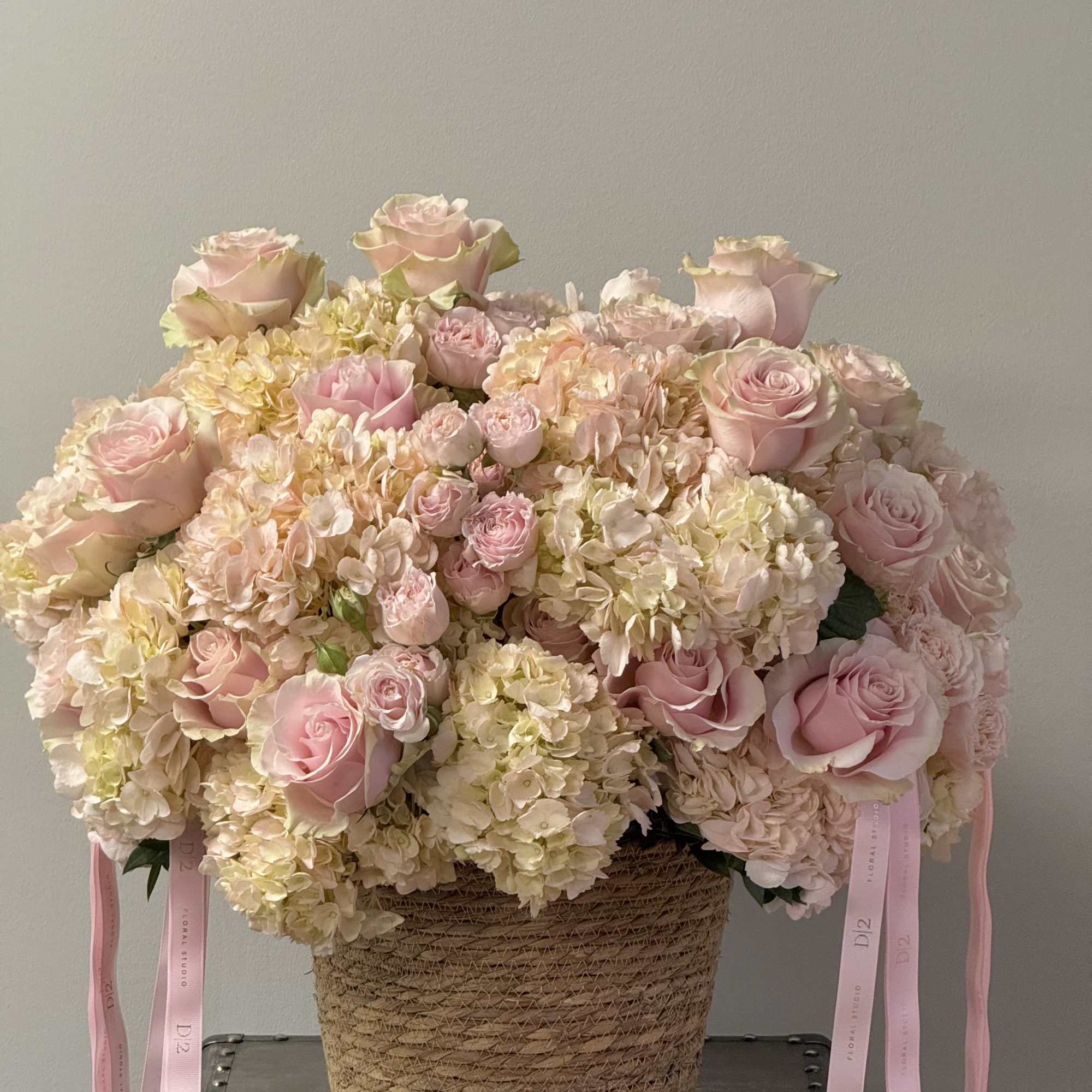 Pink roses and hydrangeas in a woven basket with ribbon tails