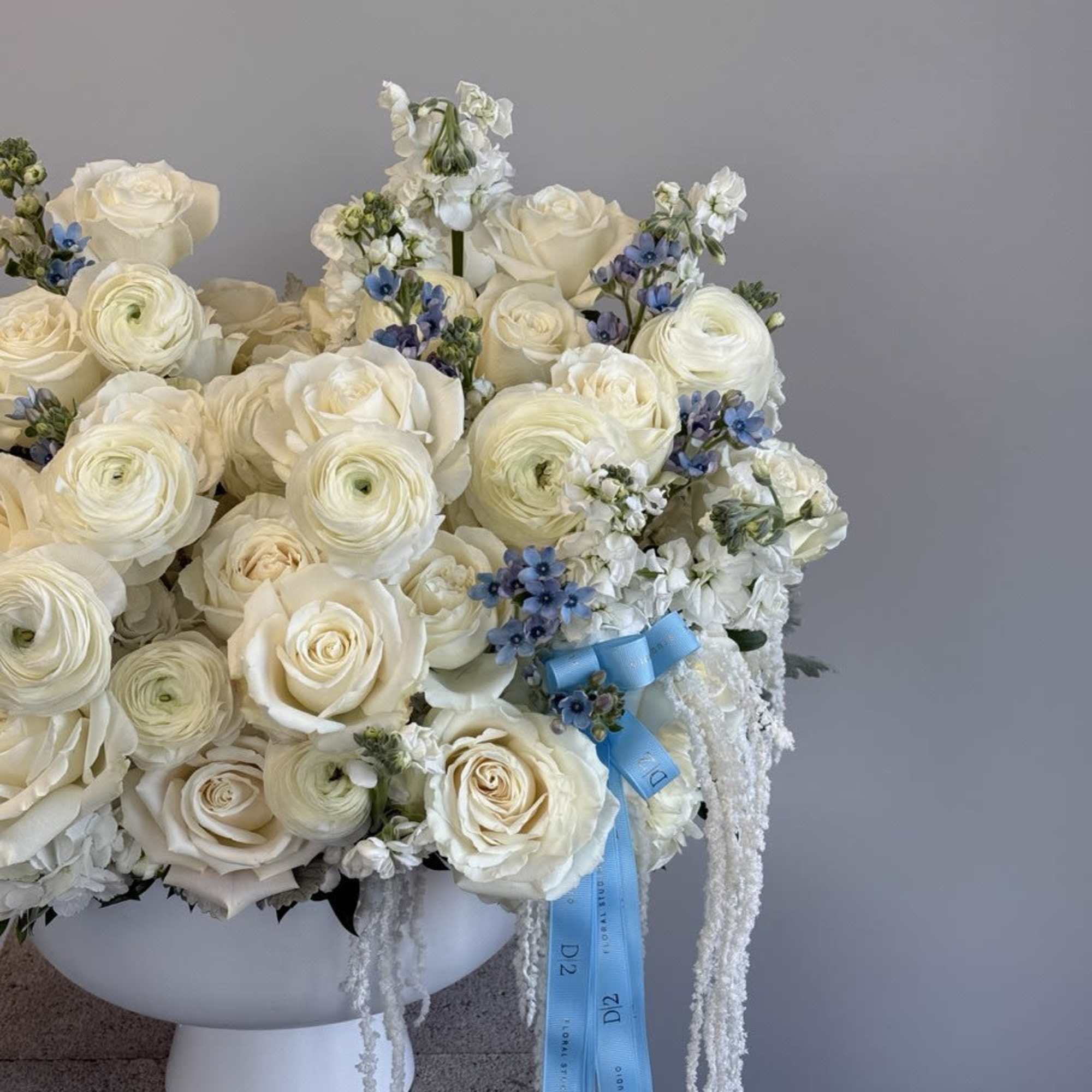 White rose and ranunculus arrangement in a white pedestal vase with blue ribbon, photo 2 of 2