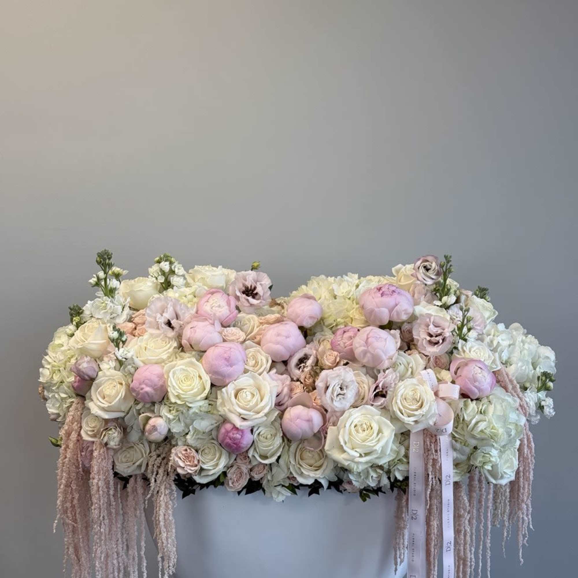Large pastel floral arrangement in a white container with trailing ribbons