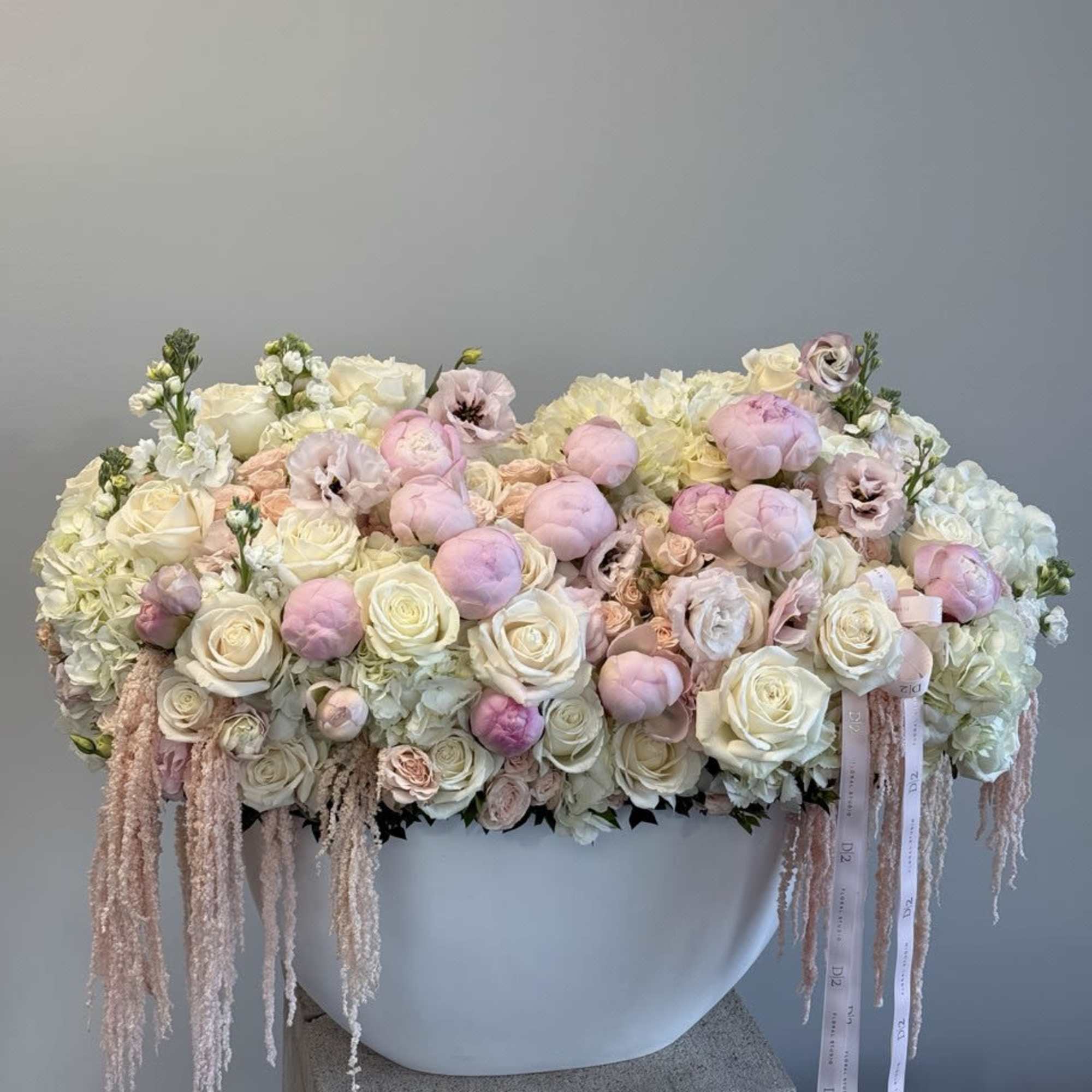 Large pastel floral arrangement in a white container with trailing ribbons, photo 3 of 3
