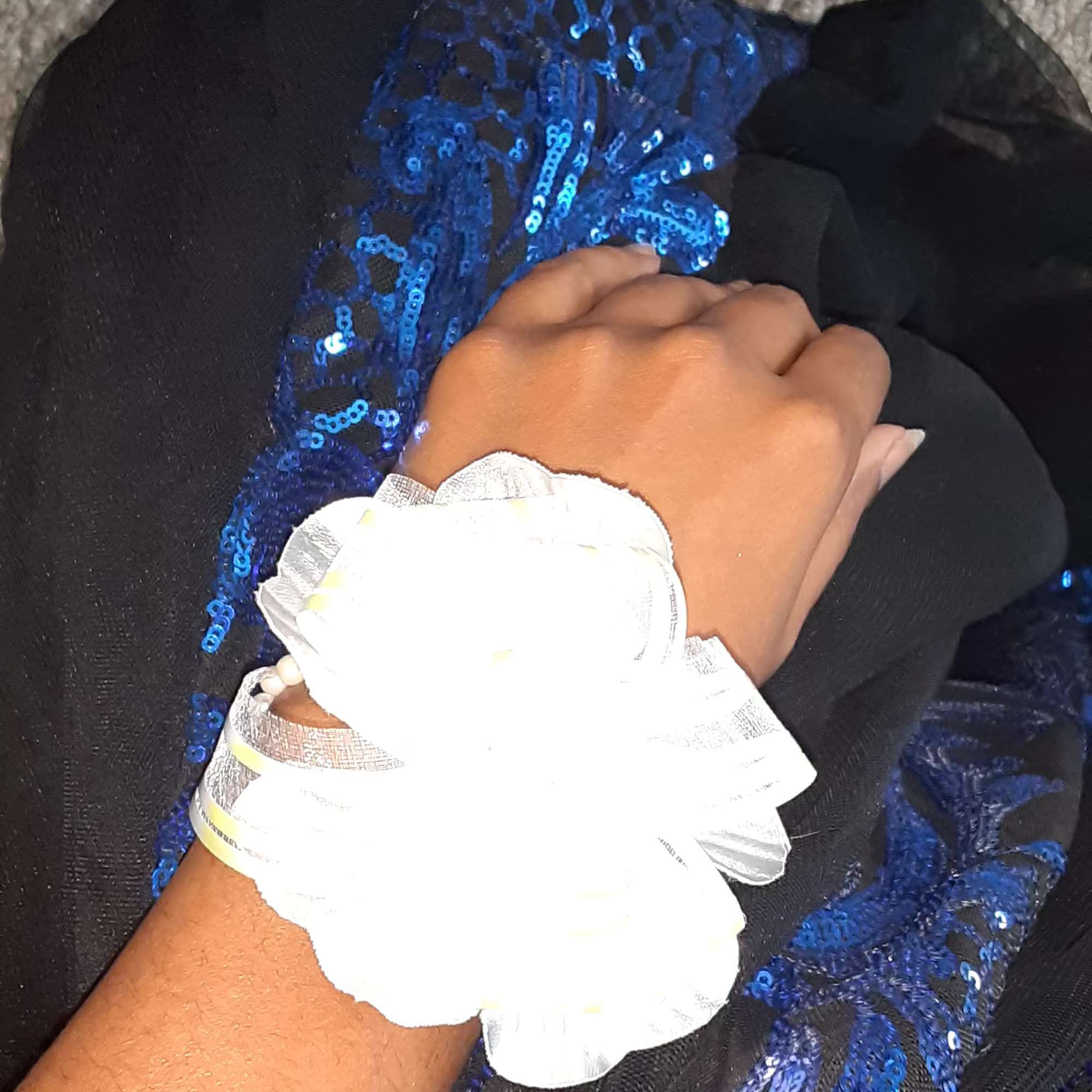 White wrist corsage on a person's wrist with a blue sequined dress