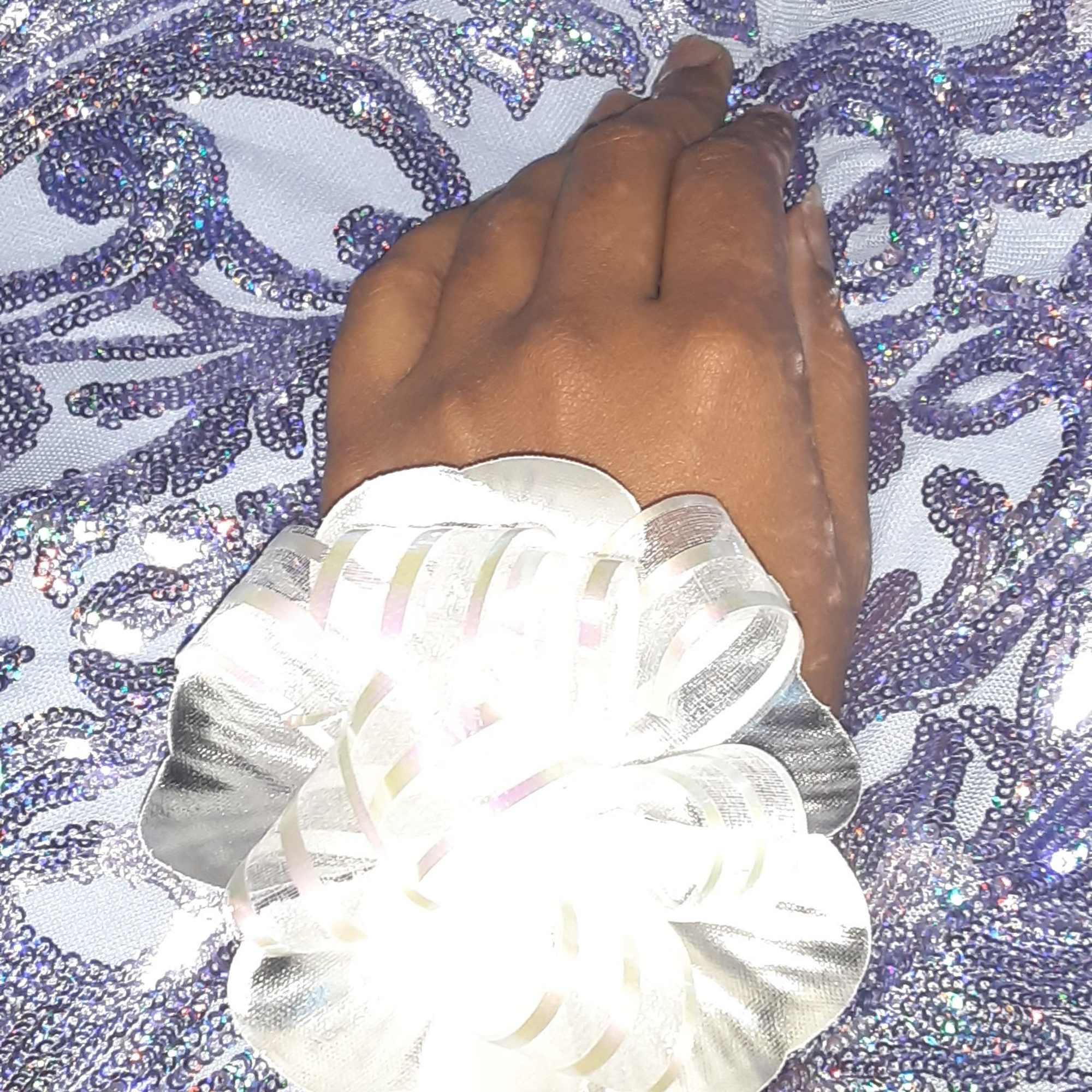 White floral wrist corsage on a hand over purple sequined fabric