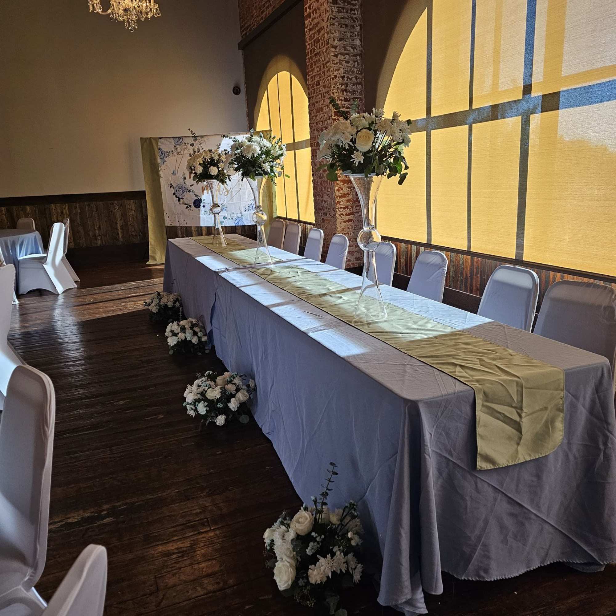 Long banquet table with tall white floral centerpieces and small floor arrangements