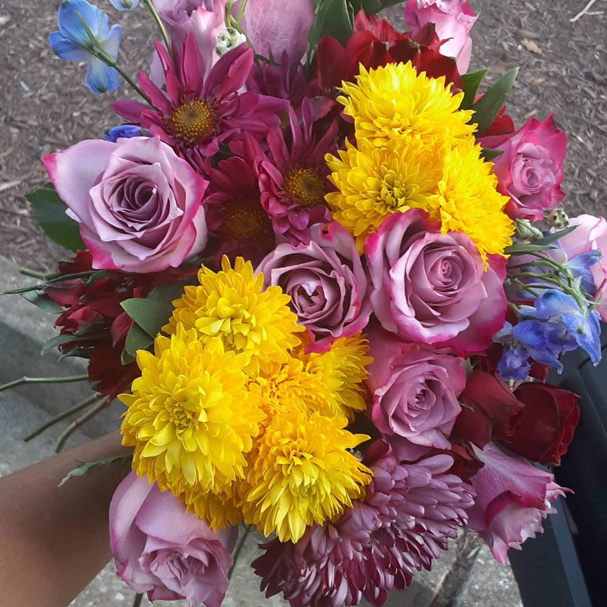 Handheld bouquet of pink roses, yellow chrysanthemums, and blue flowers