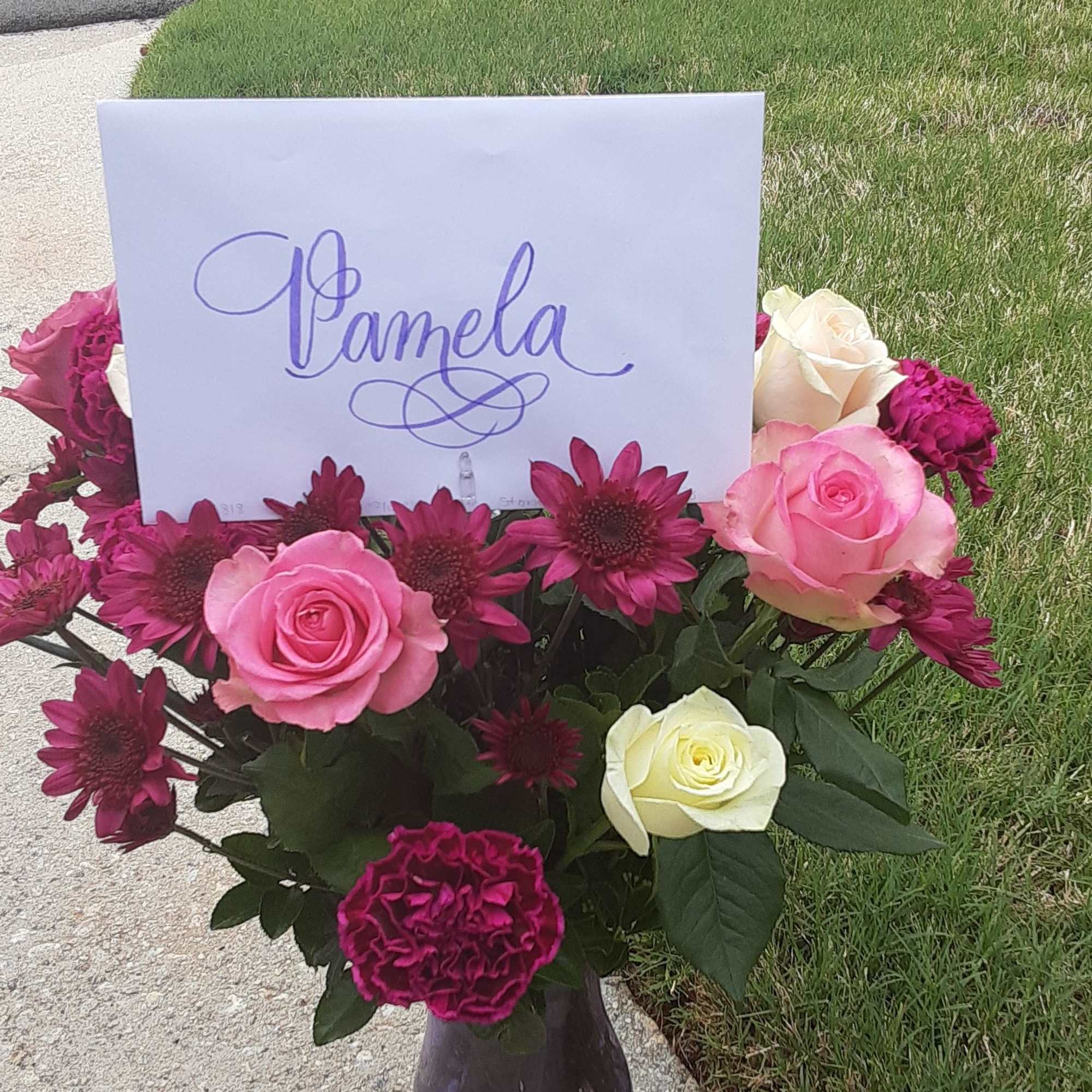 Pink and white roses with magenta daisies in a purple vase, with a name card