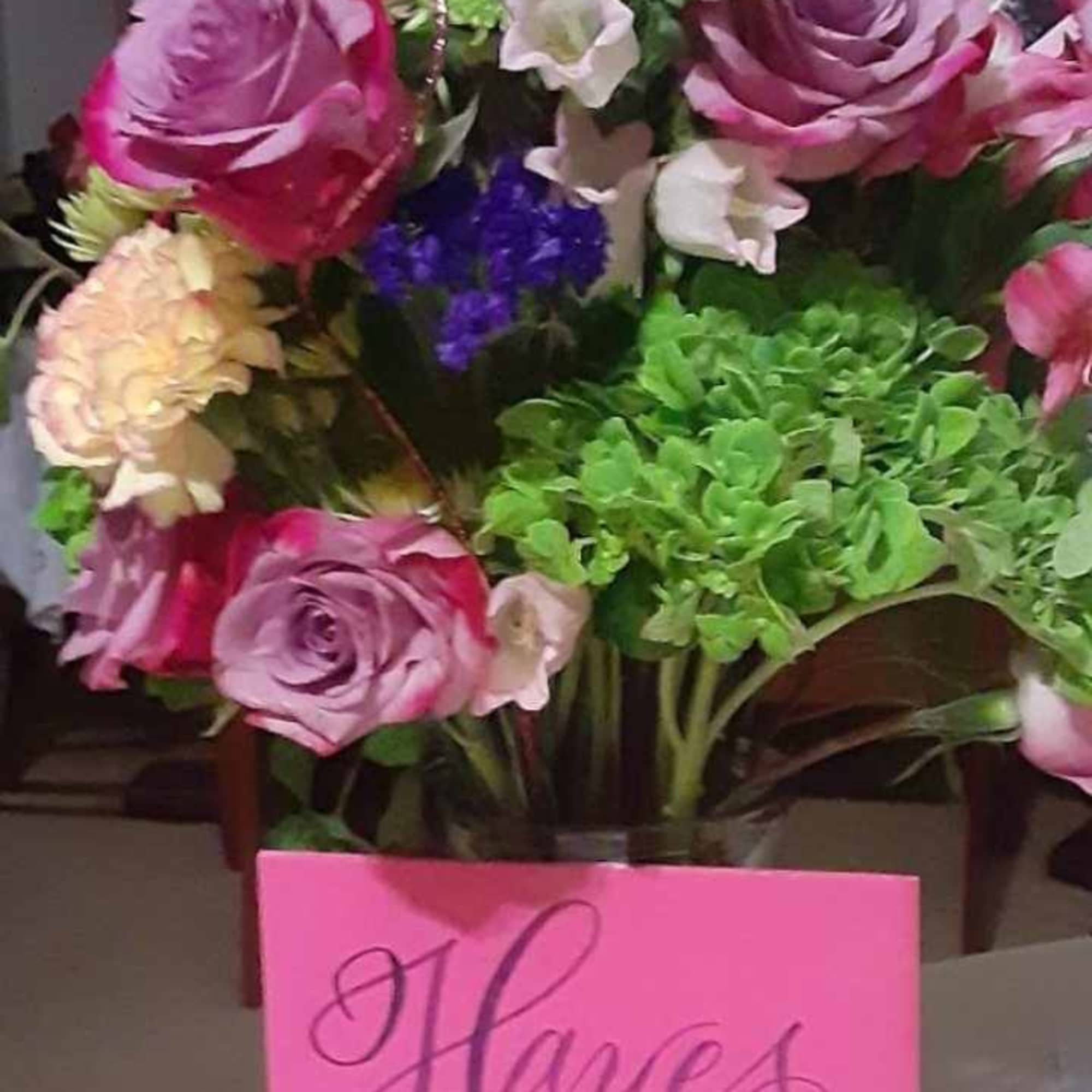 Mixed bouquet of pink and purple flowers in a glass vase with a pink card