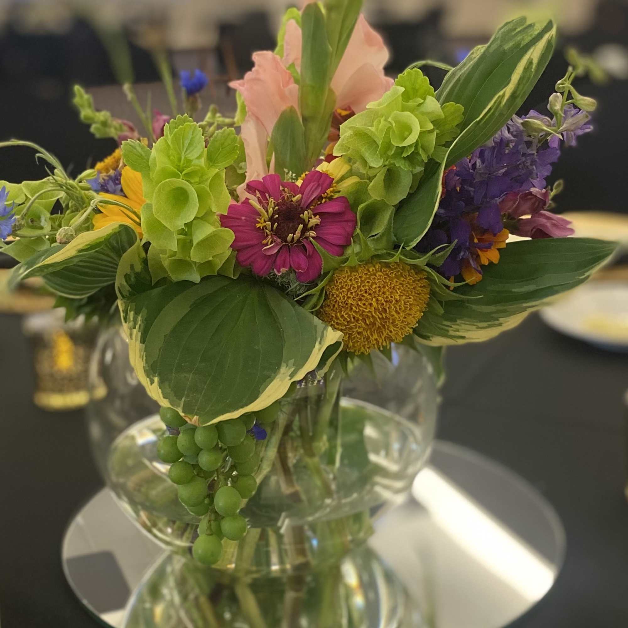 Mixed bouquet in a clear glass vase with pink, purple, yellow, and green blooms
