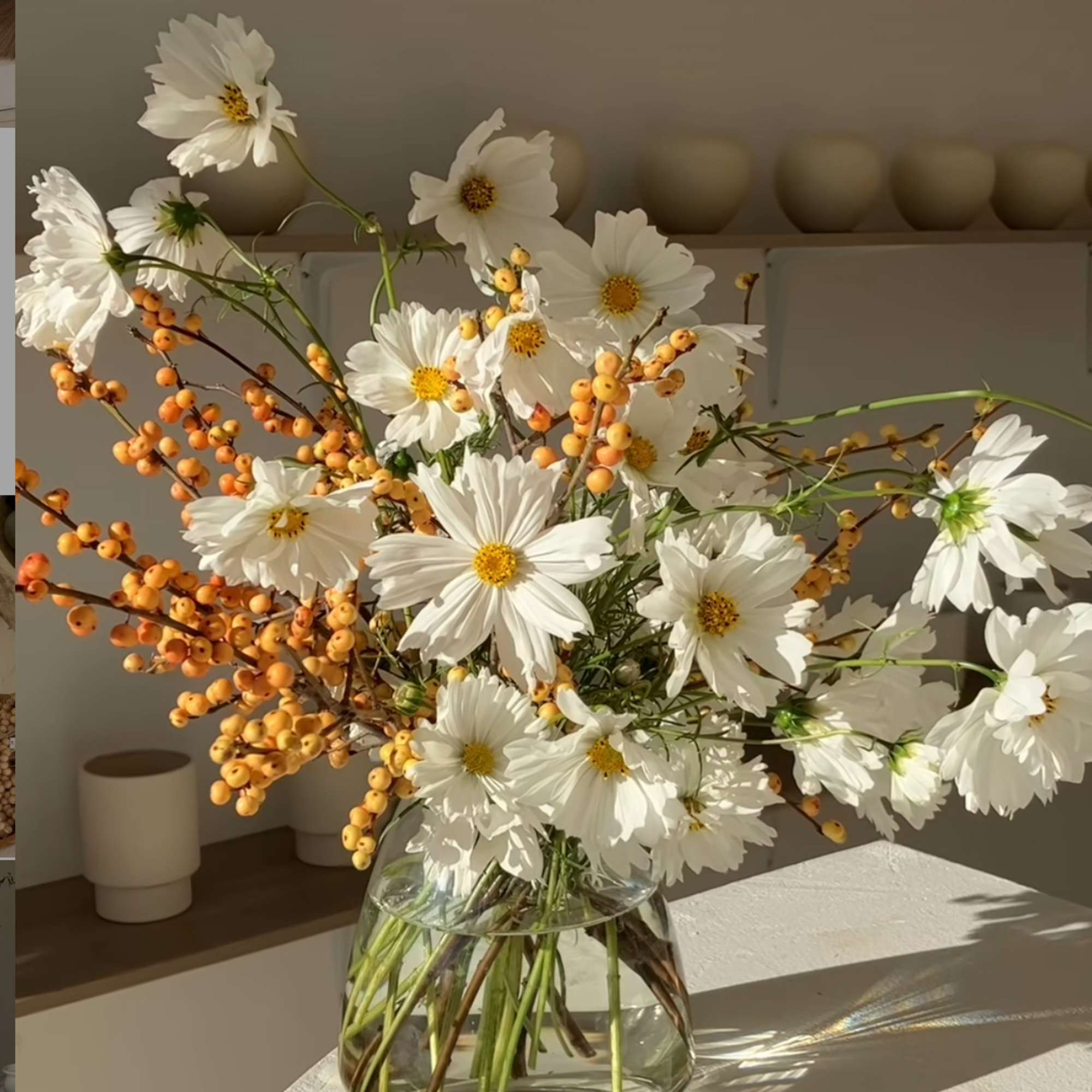 White daisy bouquet with orange berry stems in a clear glass vase