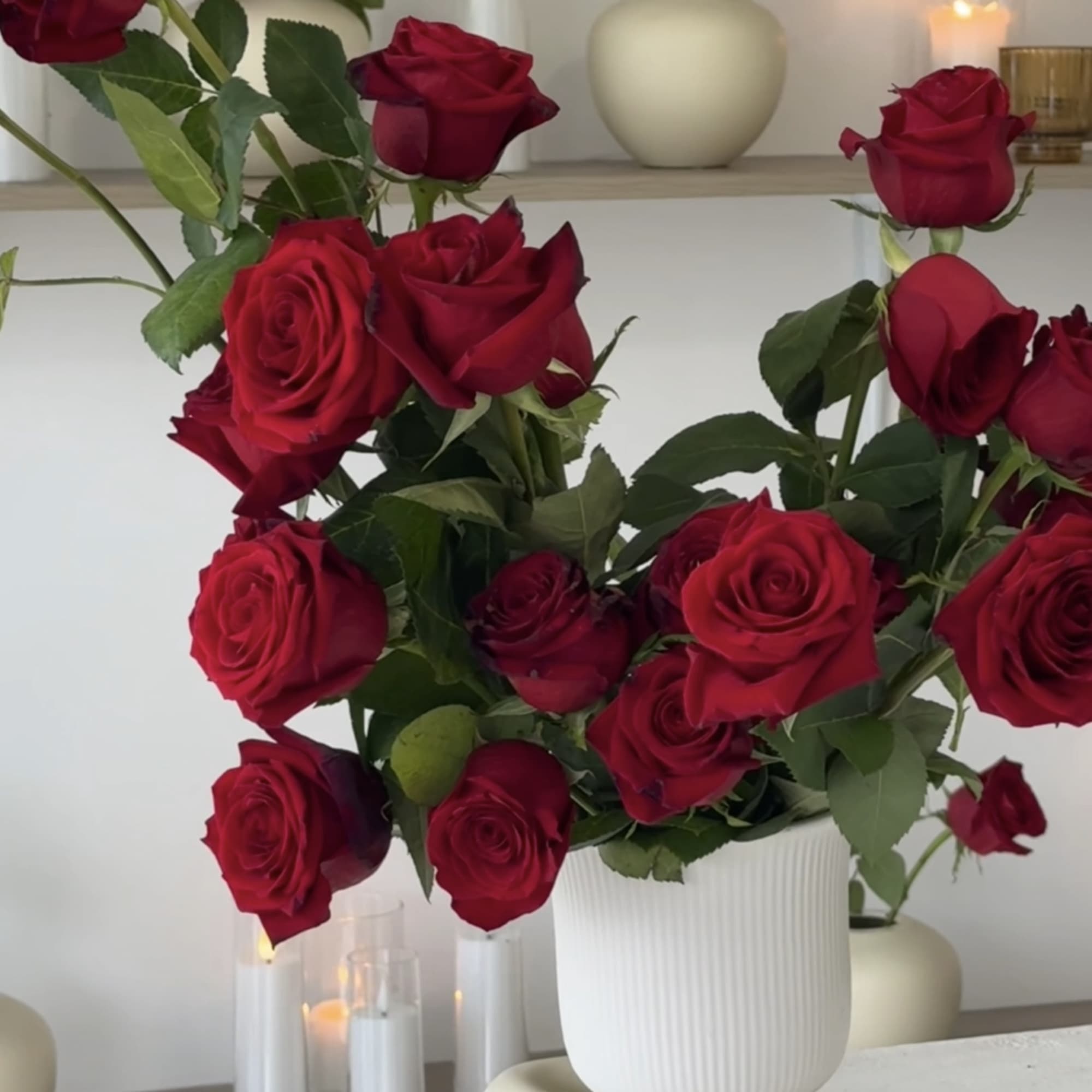 Red roses arranged in a white vase with lit candles nearby