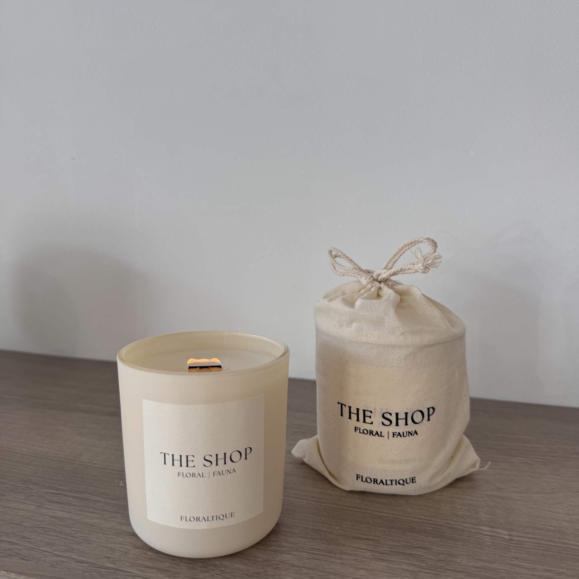 Cream candle in a glass jar beside a drawstring cloth pouch