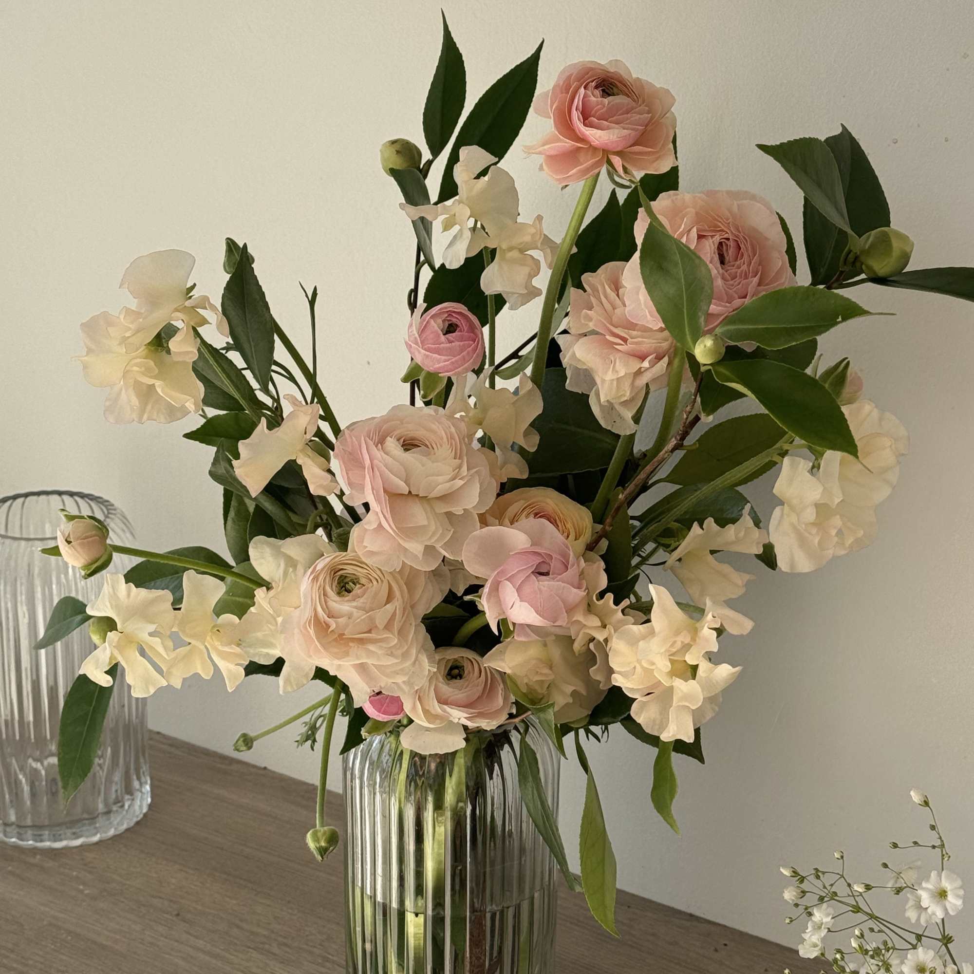 Blush pink ranunculus and white sweet pea in a clear glass vase