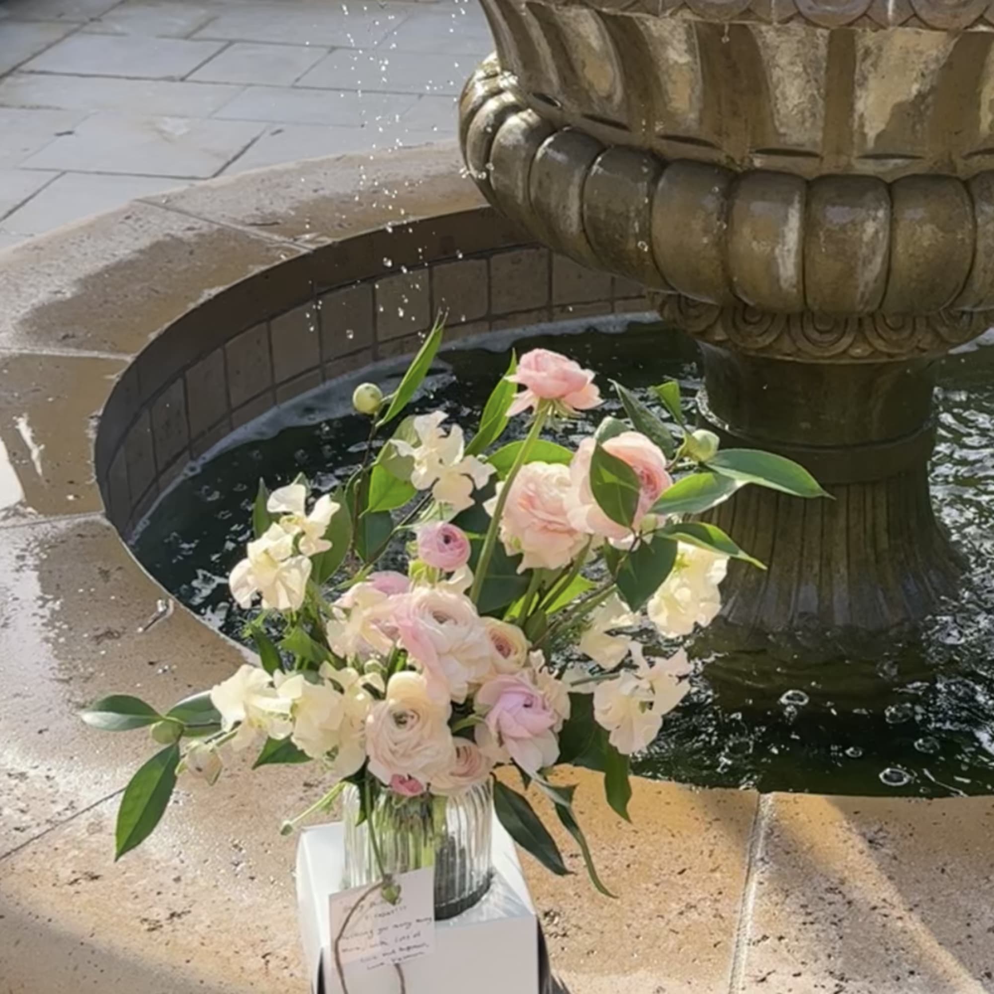 Blush and white floral arrangement in a glass vase beside a fountain