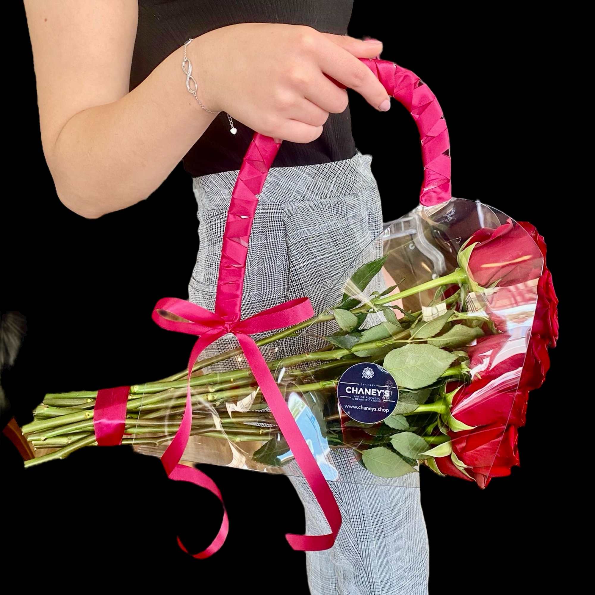 A hand holds a bouquet of red roses wrapped in clear plastic with a pink ribbon.