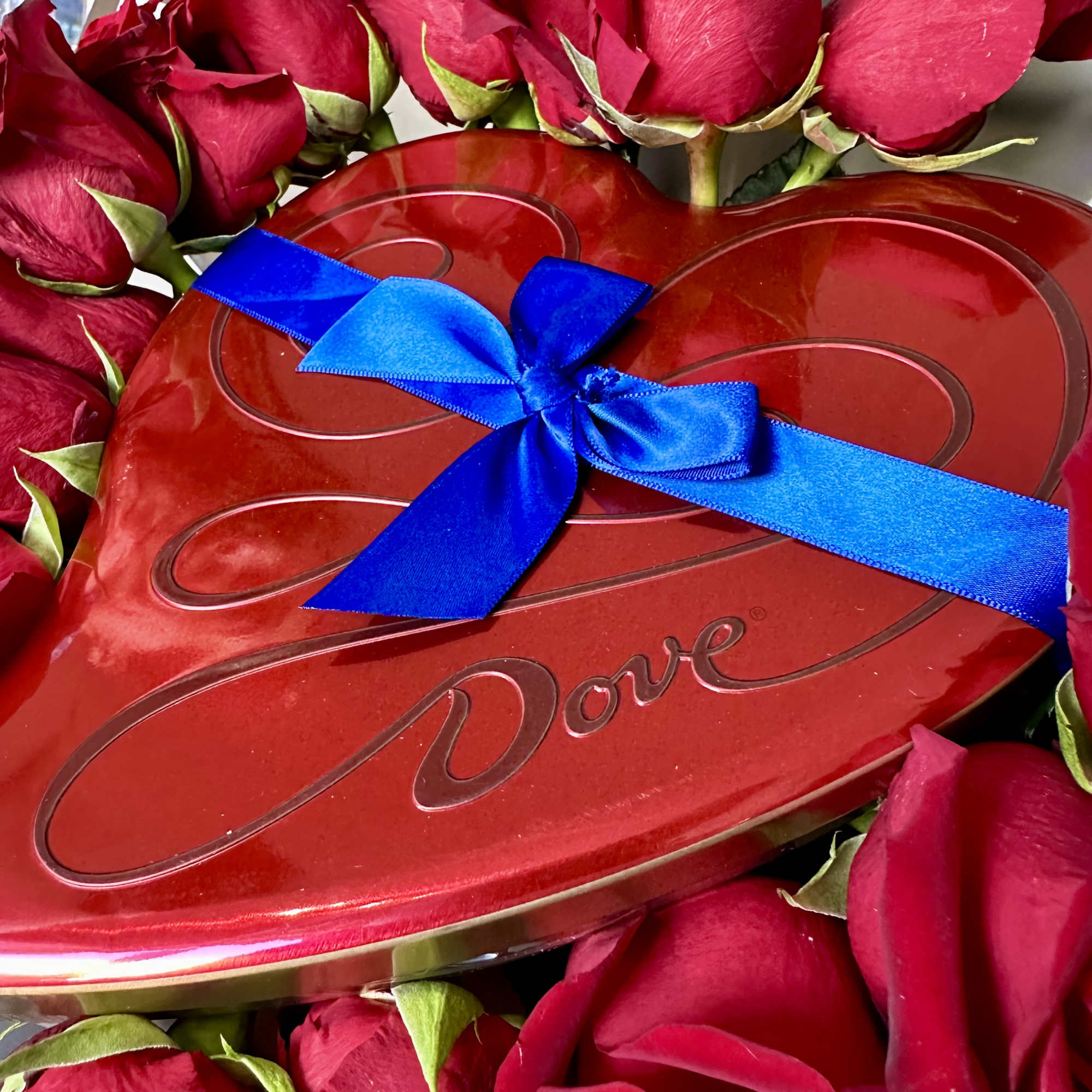 Red roses arranged around a heart-shaped Dove chocolate box tied with a blue ribbon.