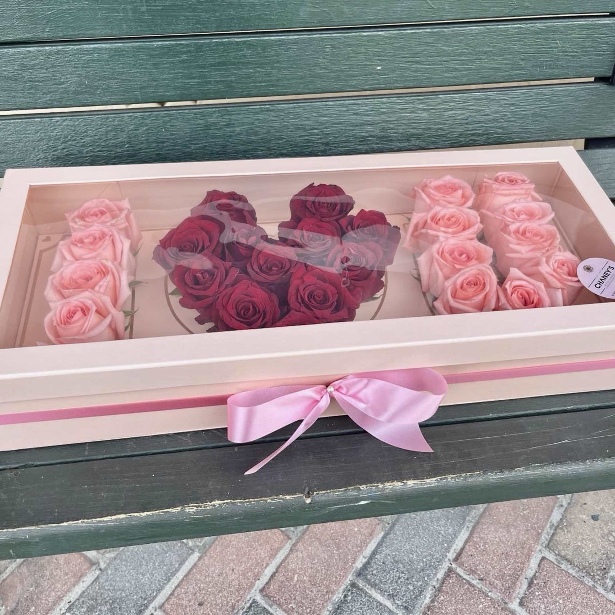 Pink and burgundy roses arranged in a gift box with a ribbon.