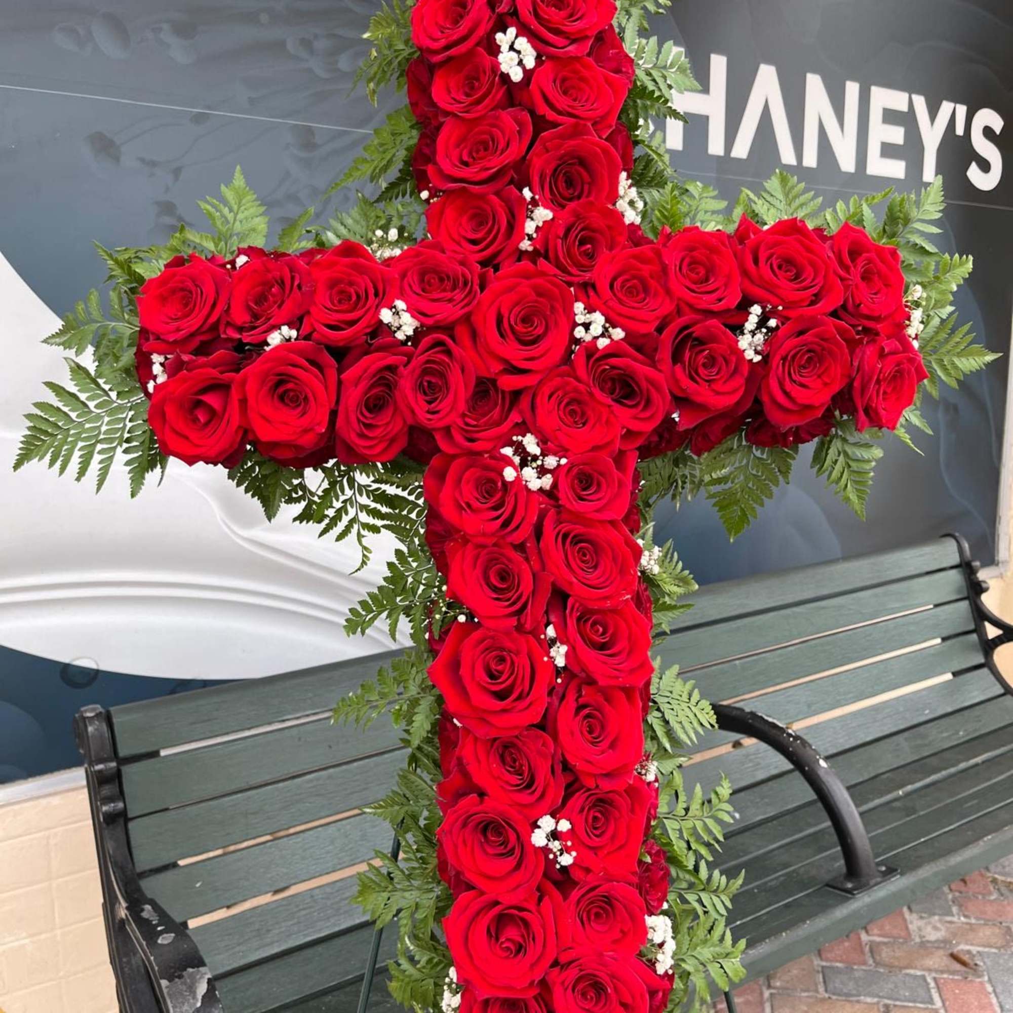 Cross-shaped arrangement of red roses with greenery and white filler flowers