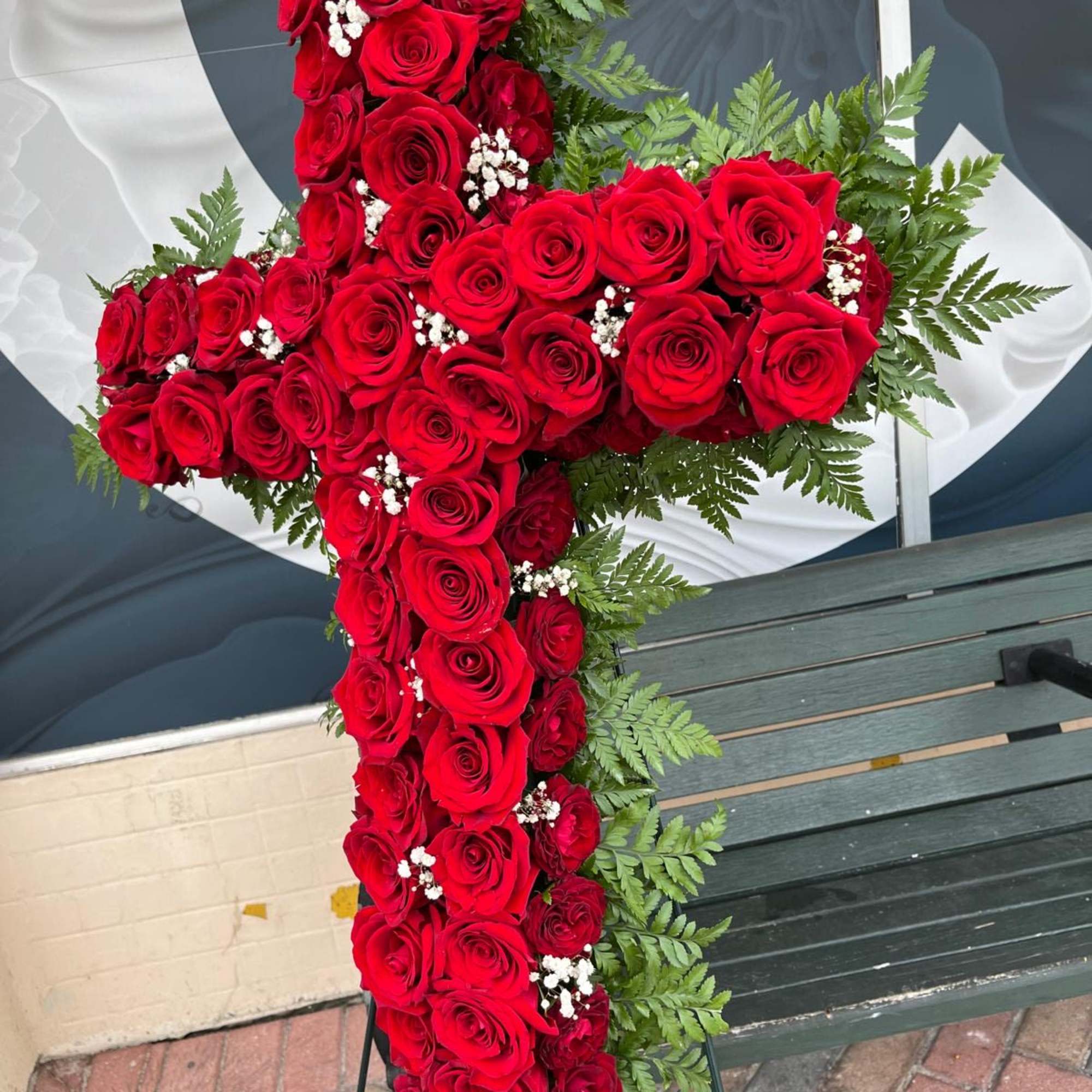 Cross-shaped arrangement of red roses with fern accents