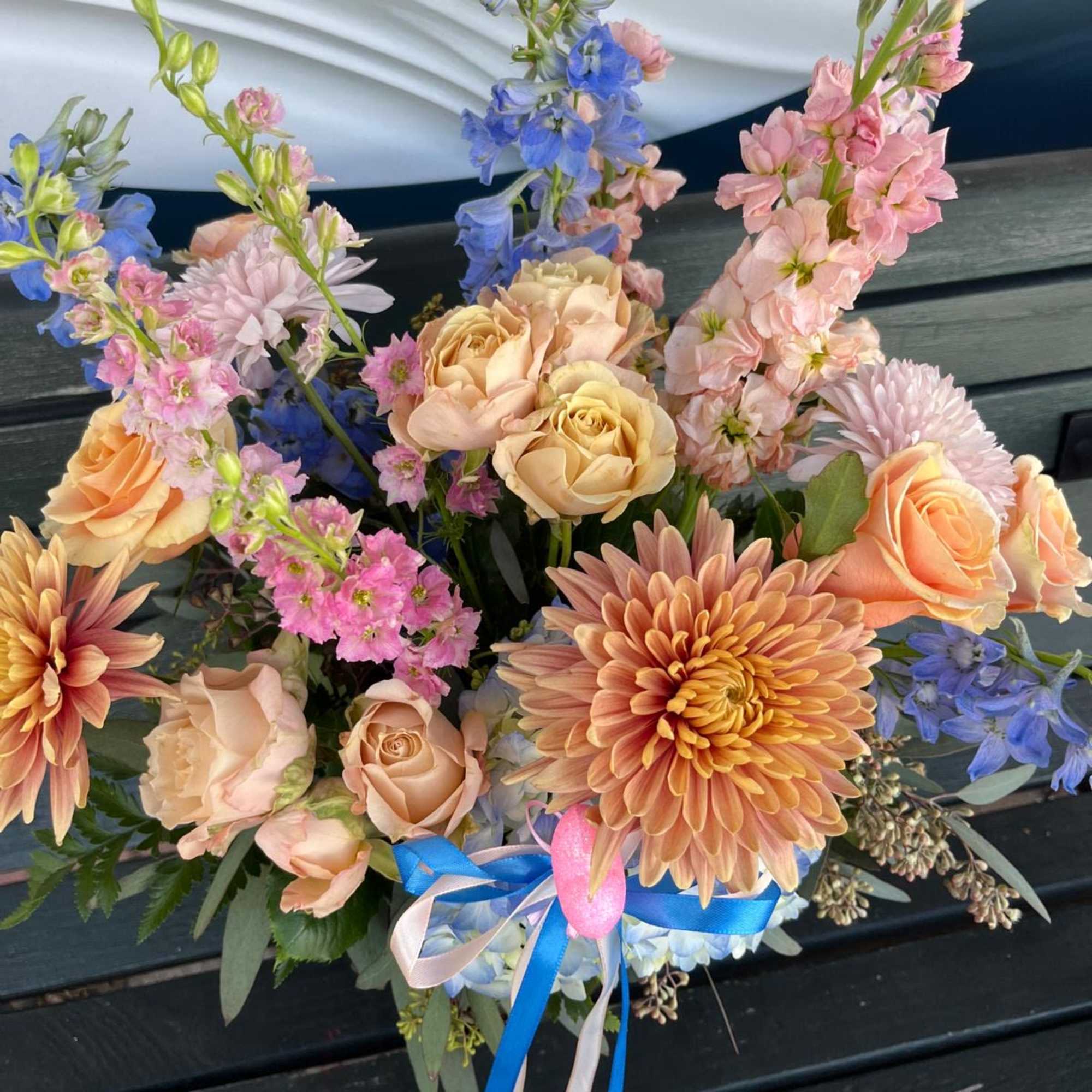 Bouquet of peach roses, blue delphinium, and pink blooms tied with ribbon