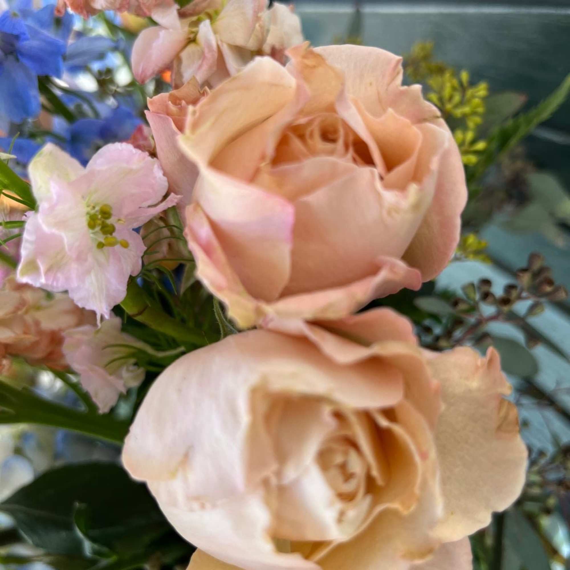 Peach roses with pale pink and blue flowers in a bouquet