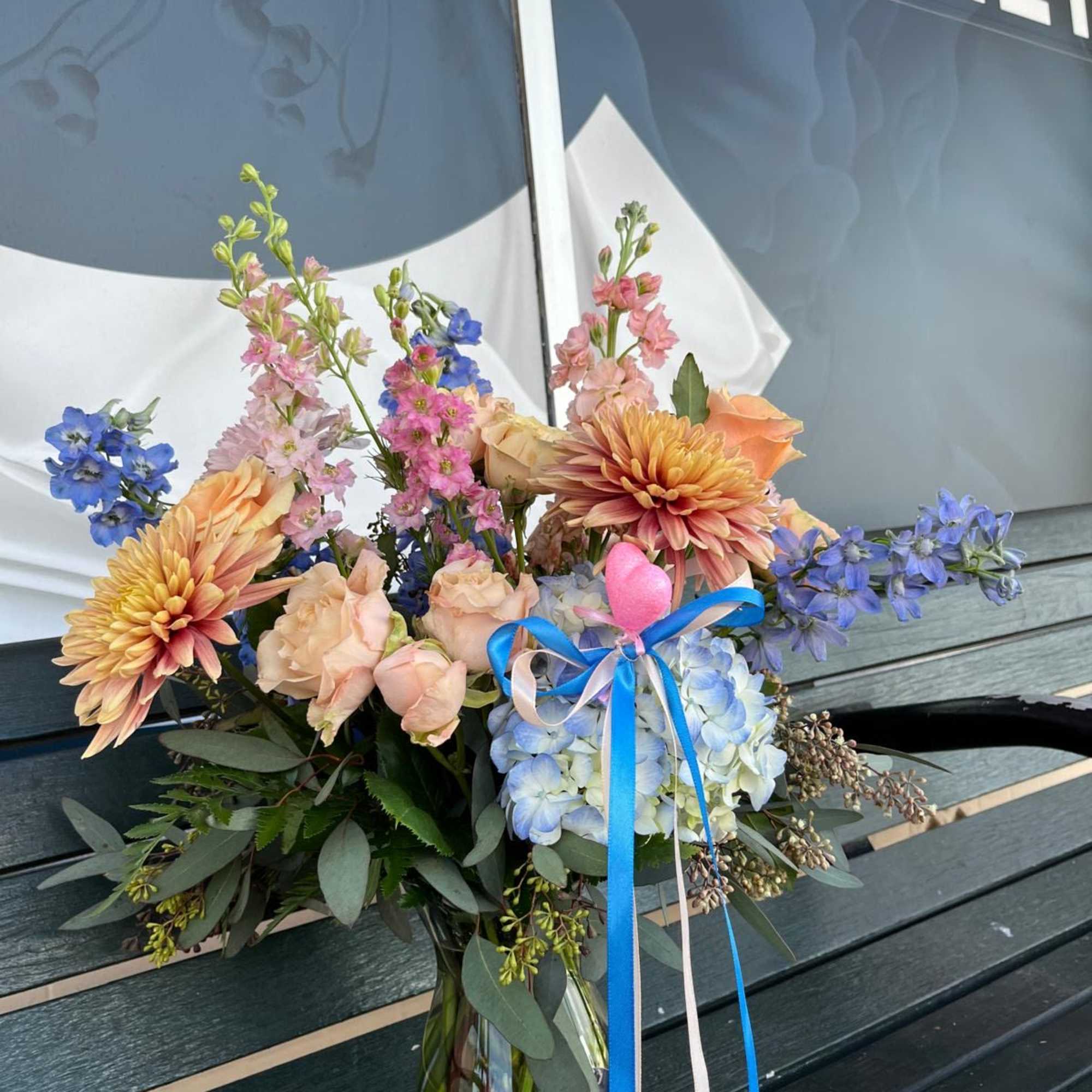 Mixed bouquet in a glass vase with blue, peach, and pink flowers