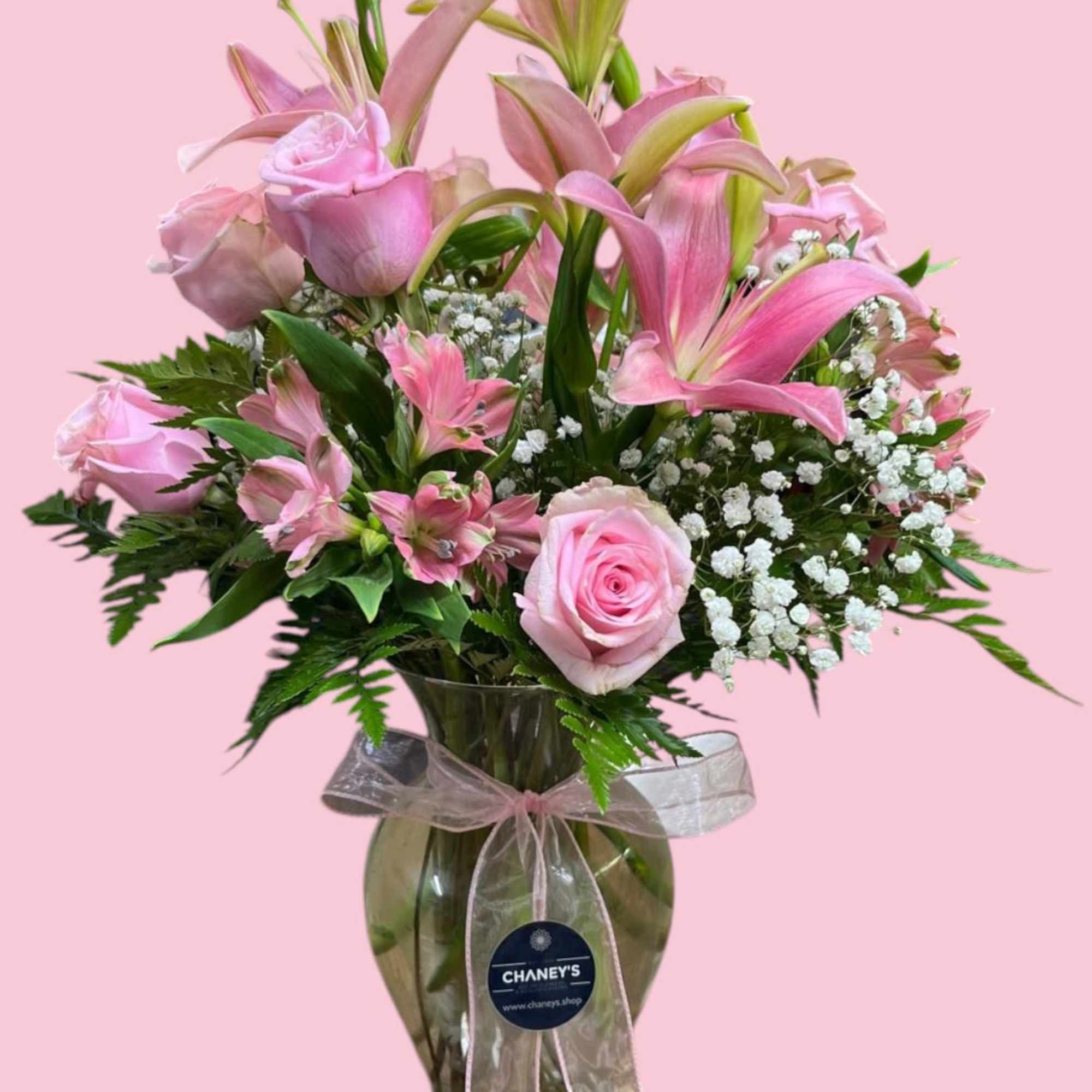 Pink roses and lilies arranged in a glass vase with a ribbon