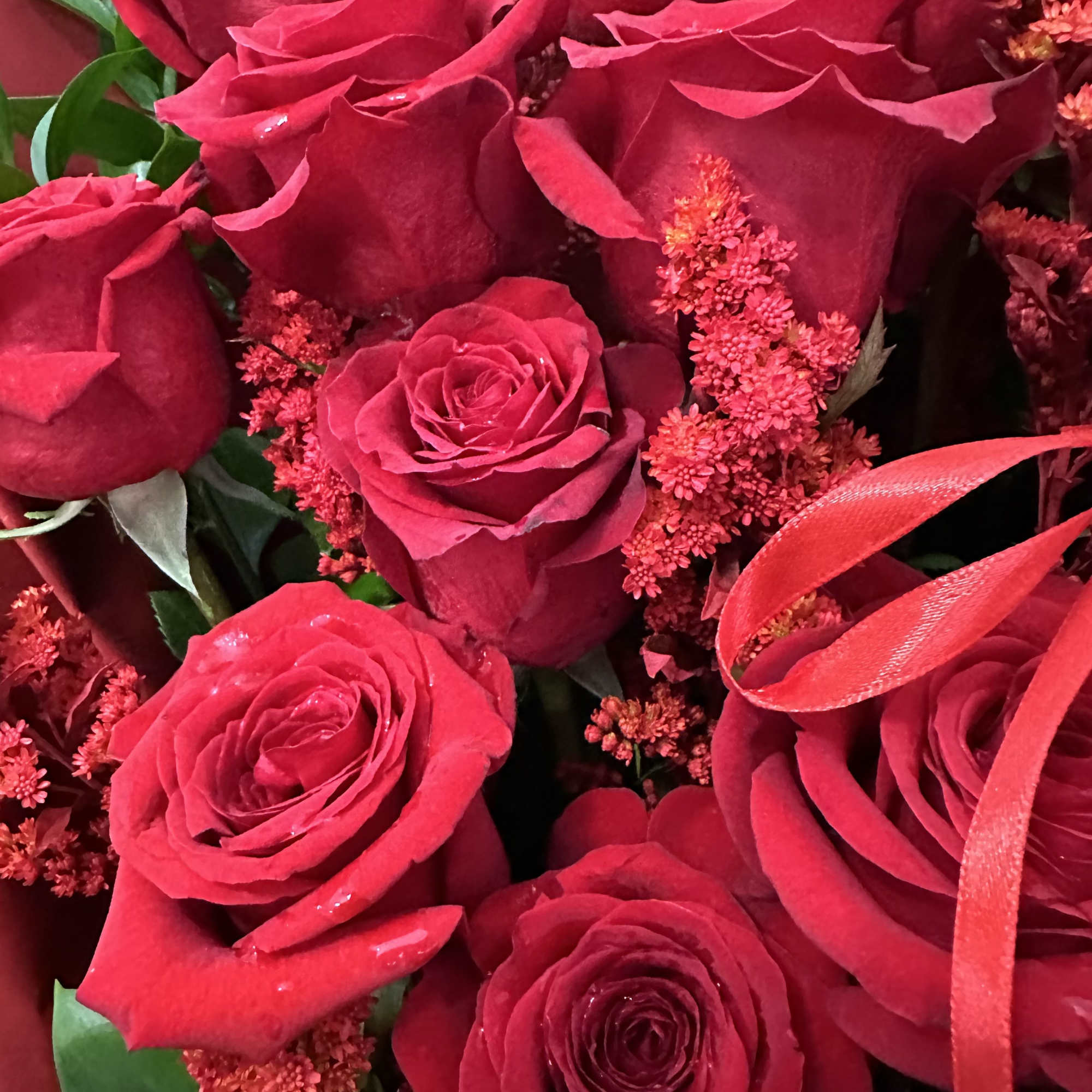 Close-up bouquet of red roses with small red filler flowers and ribbon