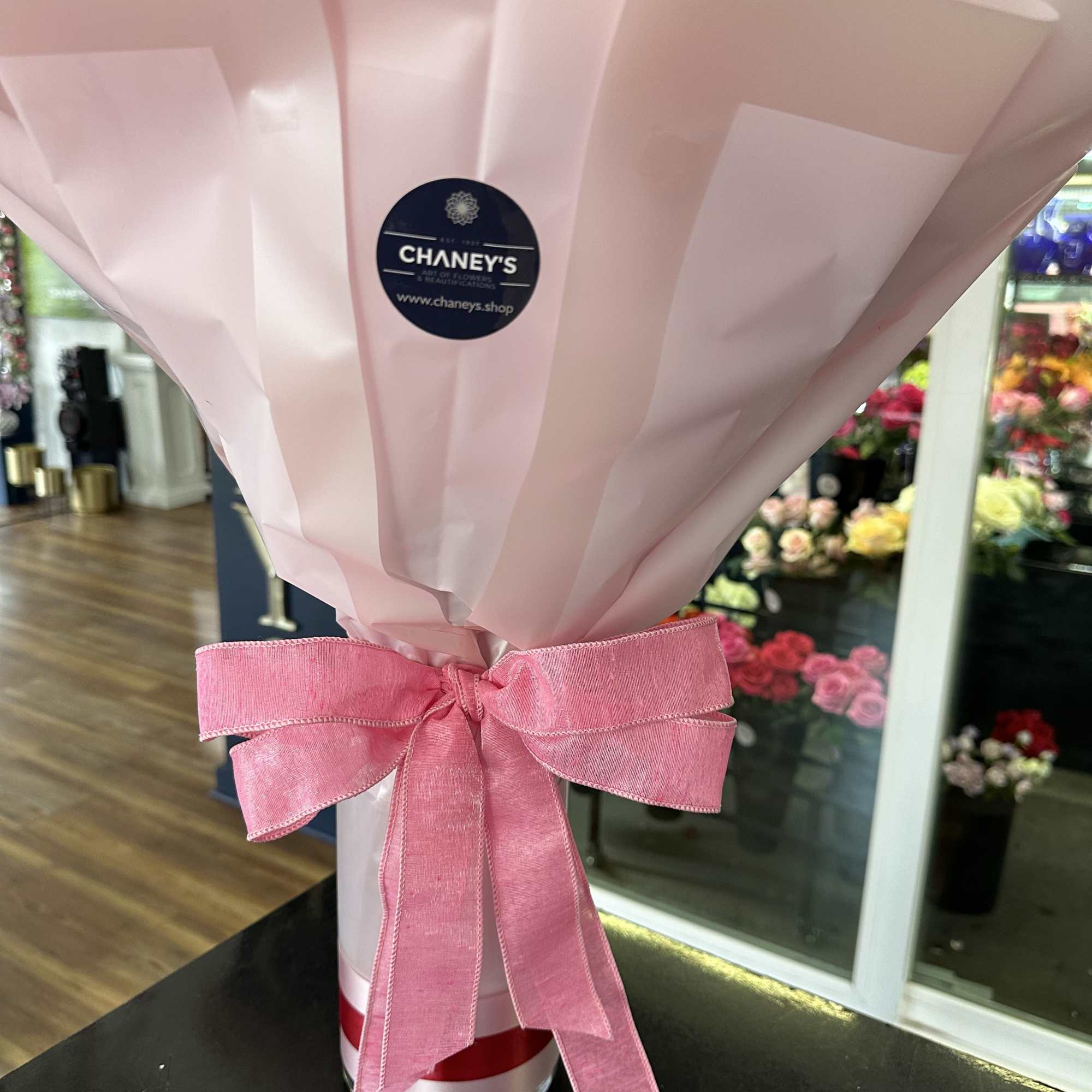 Pink-wrapped bouquet with a large pink ribbon in a glass vase