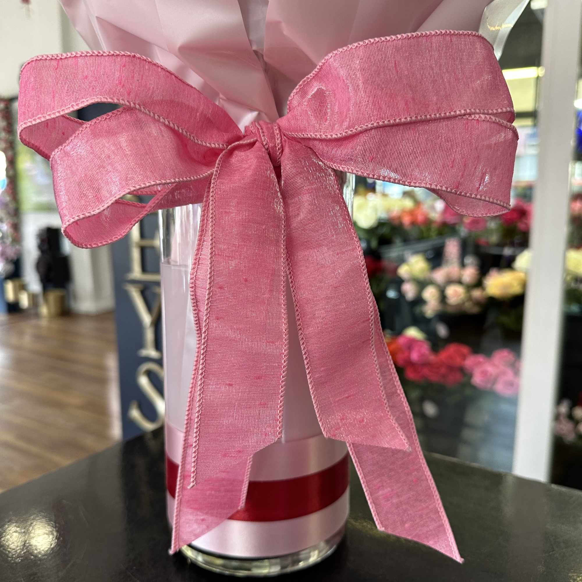 Clear vase wrapped in pink paper with a large pink ribbon bow