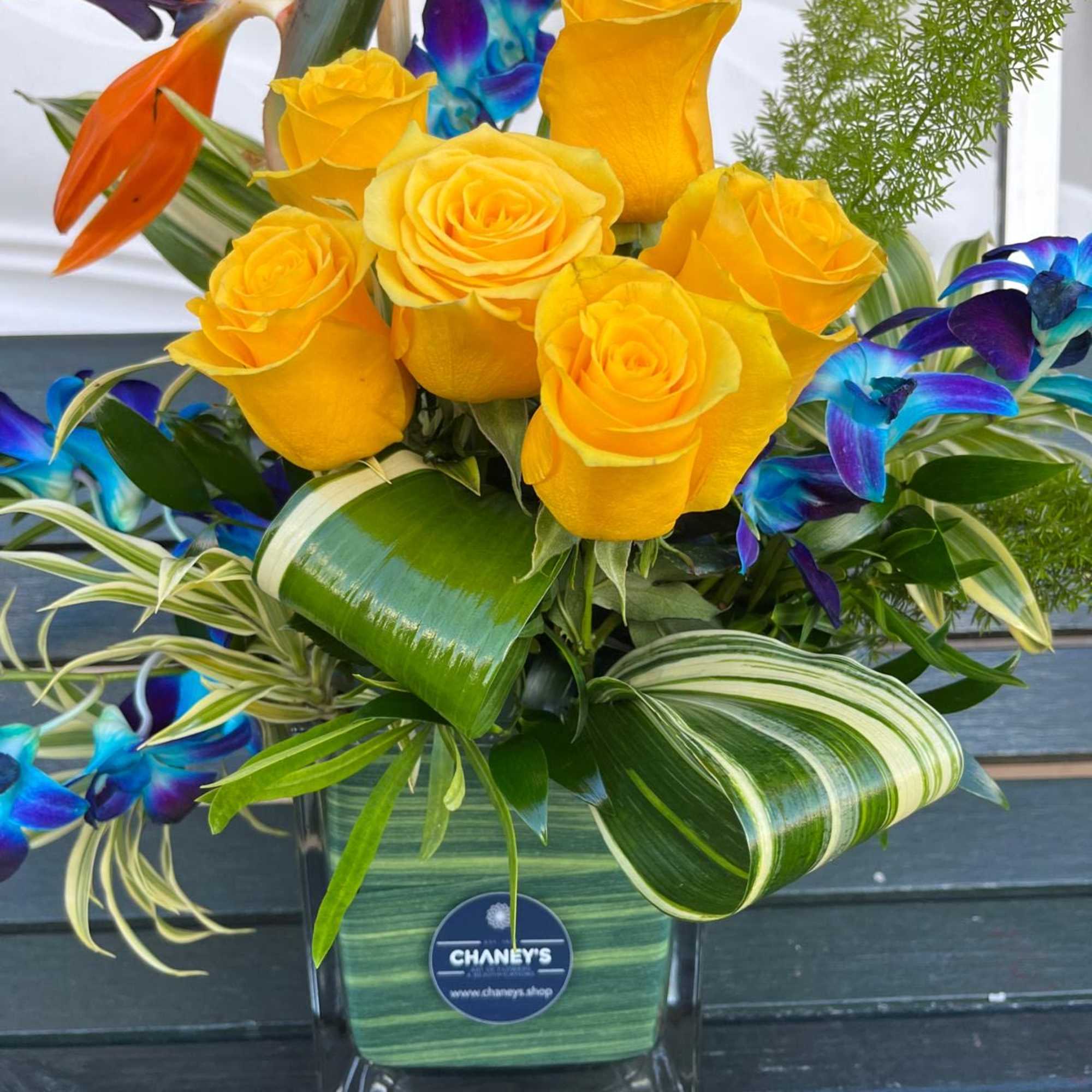 Yellow roses in a glass vase with tropical blue and orange flowers