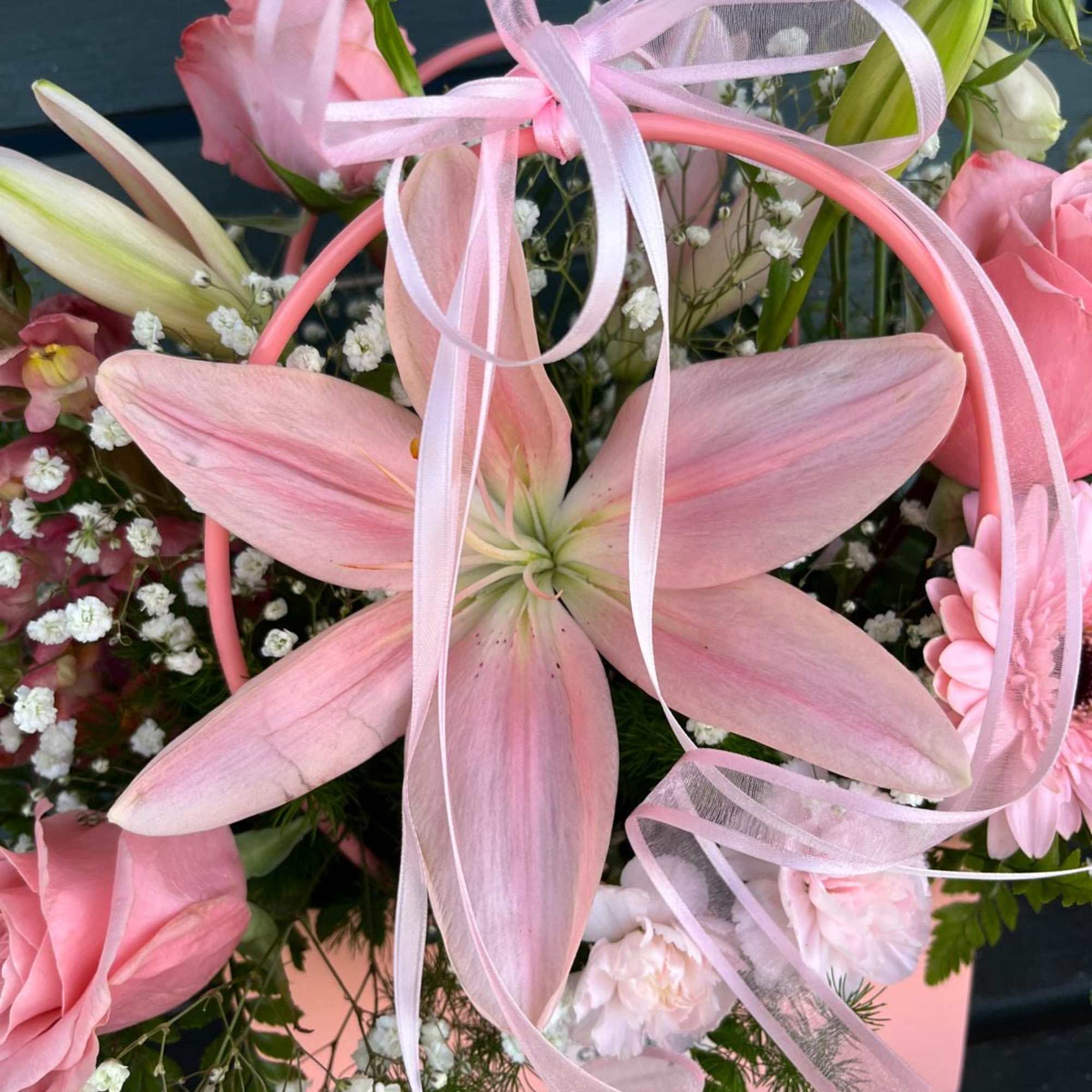 Pink lilies and roses in a pink basket with ribbon