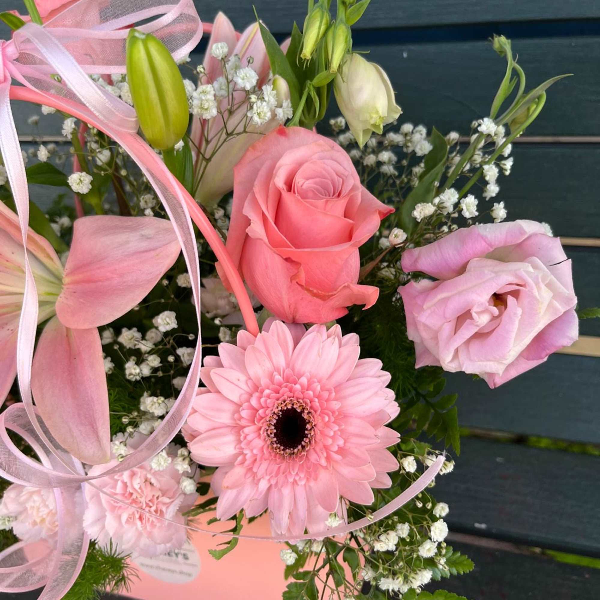 Pink bouquet with roses, a gerbera daisy, and lilies tied with ribbon