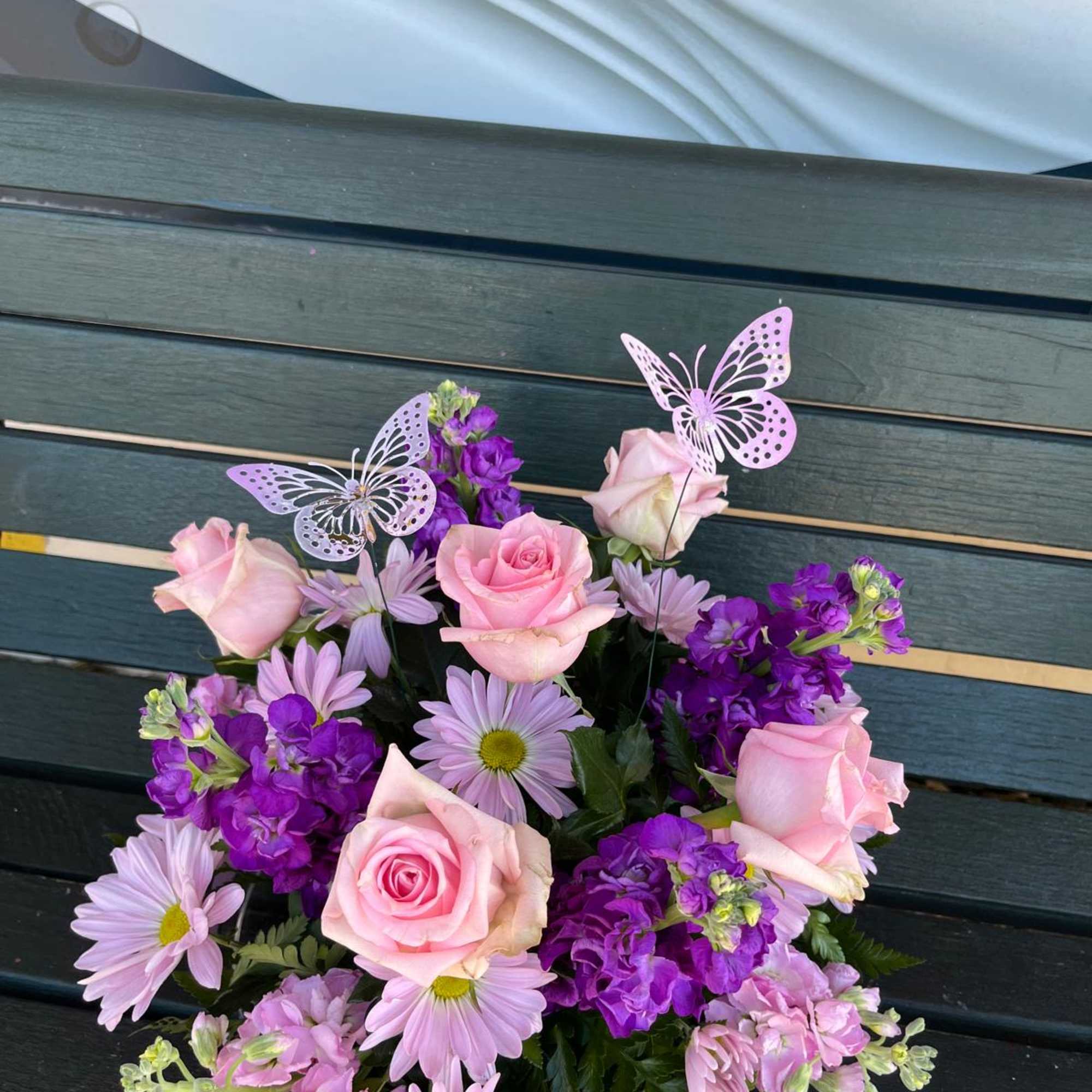 Pink roses and purple daisies arranged with butterfly picks