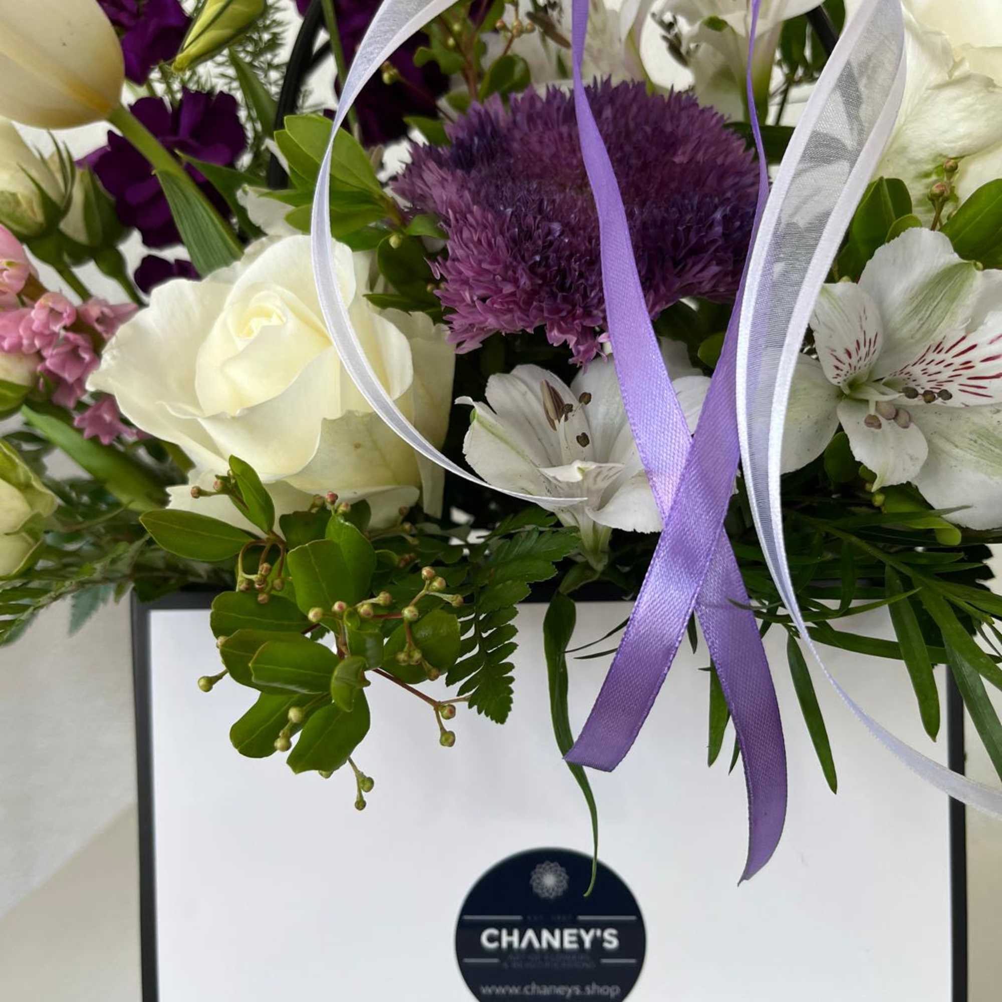 White and purple floral arrangement in a gift box with ribbon