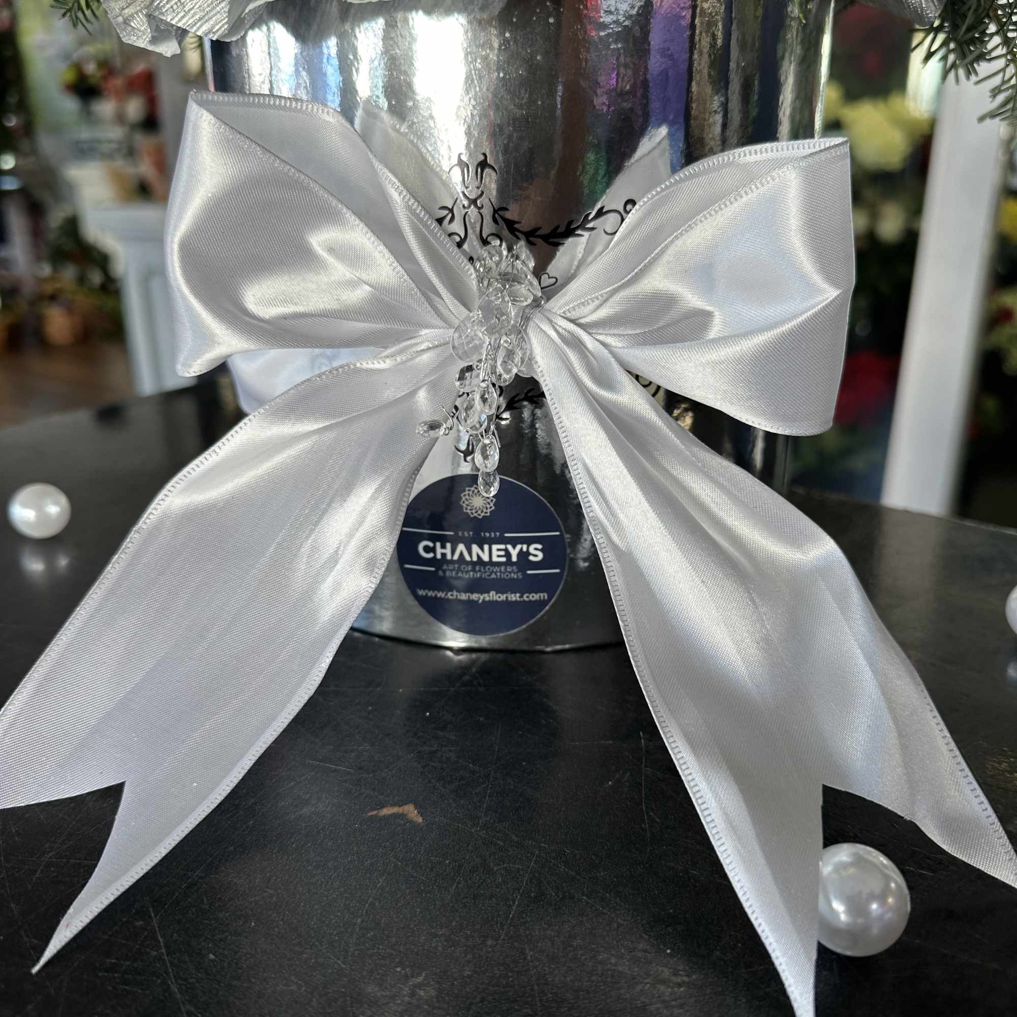 Silver gift bucket with a large white satin bow and greenery trim