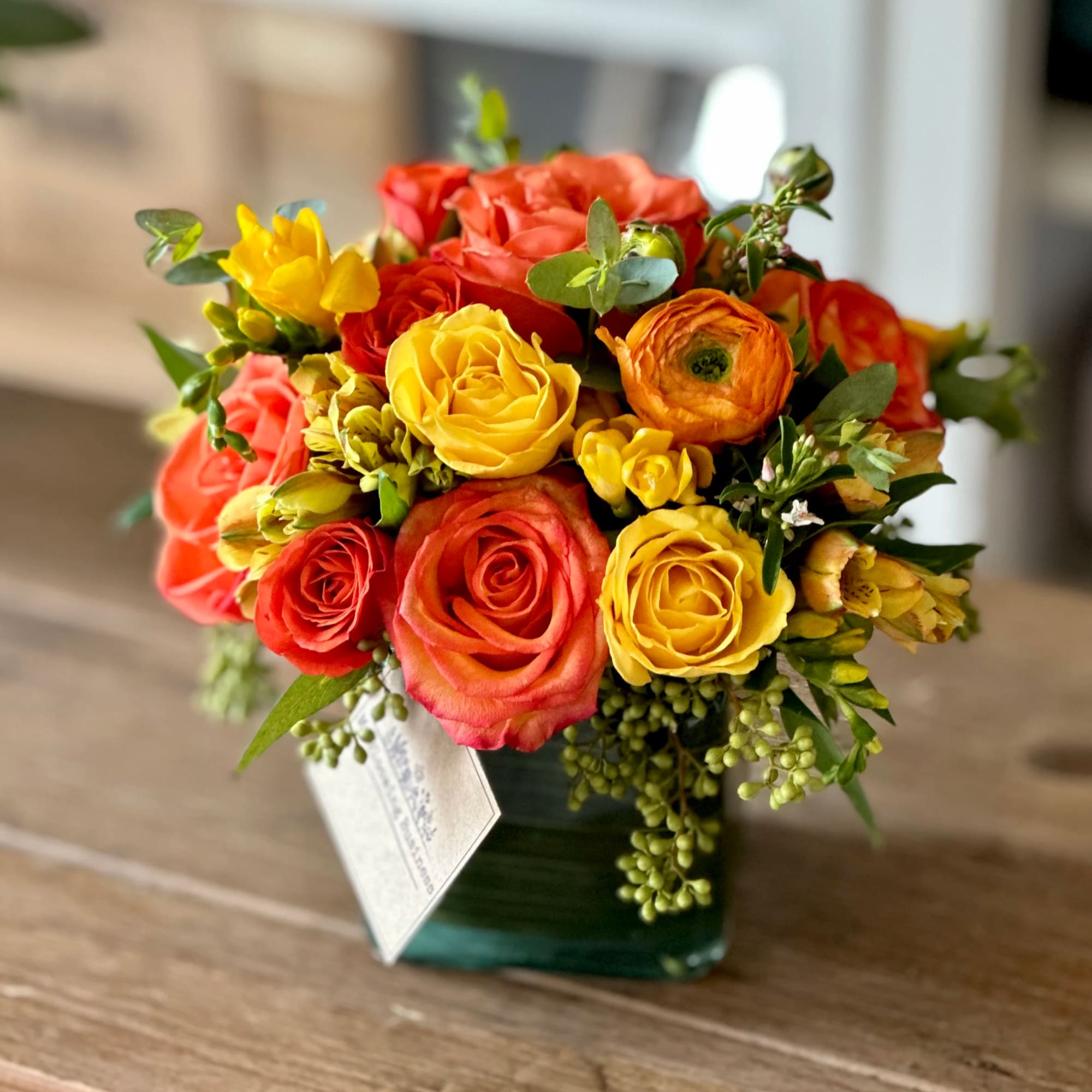 Bouquet of yellow, orange, and coral roses in a square glass vase